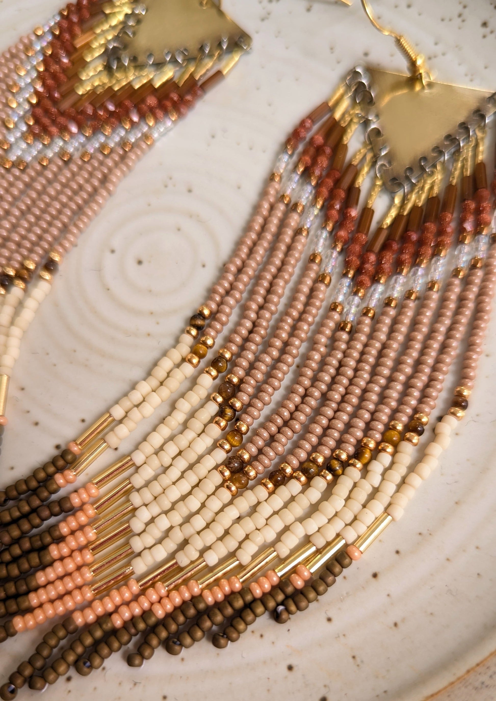 Long handcrafted fringe earrings by Moon & Milk with warm terracotta, beige, and ivory seed beads, finished with brass triangle tops and fine detailing.