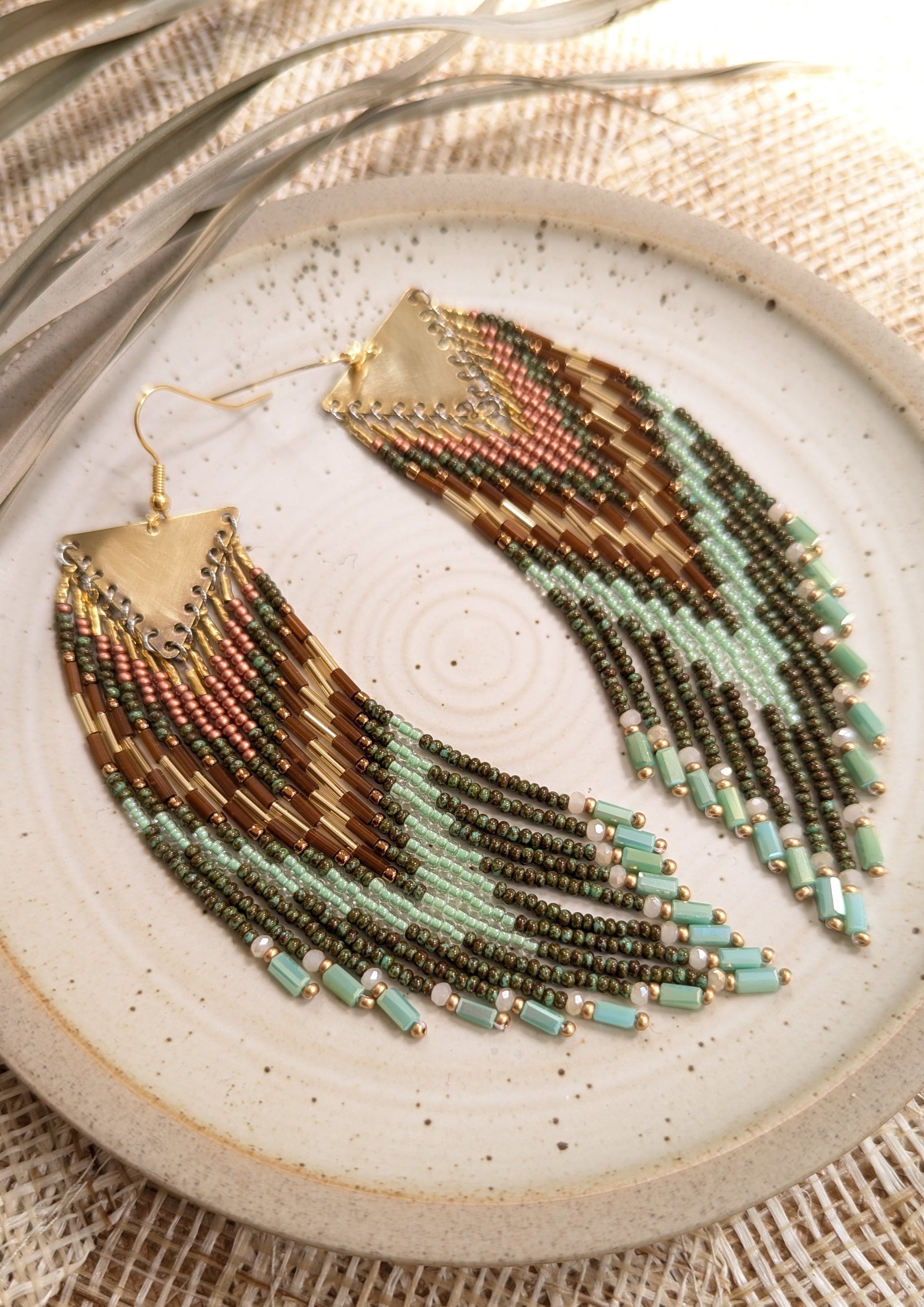 Moon & Milk handcrafted fringe earrings with olive green, mint, and bronze seed beads and brass findings, displayed on a ceramic plate in natural light.