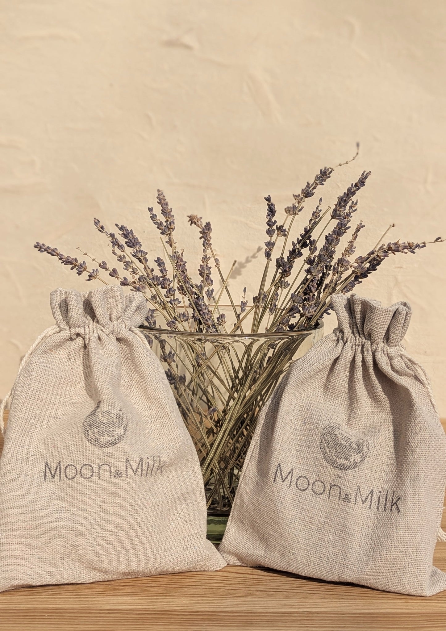 Two Moon & Milk linen jewelry pouches displayed in front of a glass jar filled with dried lavender, photographed against a neutral textured background.