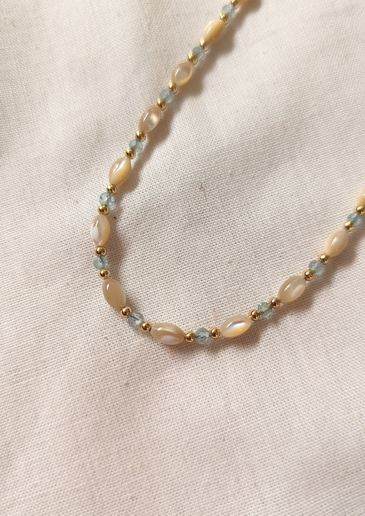 Necklace with mother-of-pearl beads and apatite aqua stones on a beige fabric background.