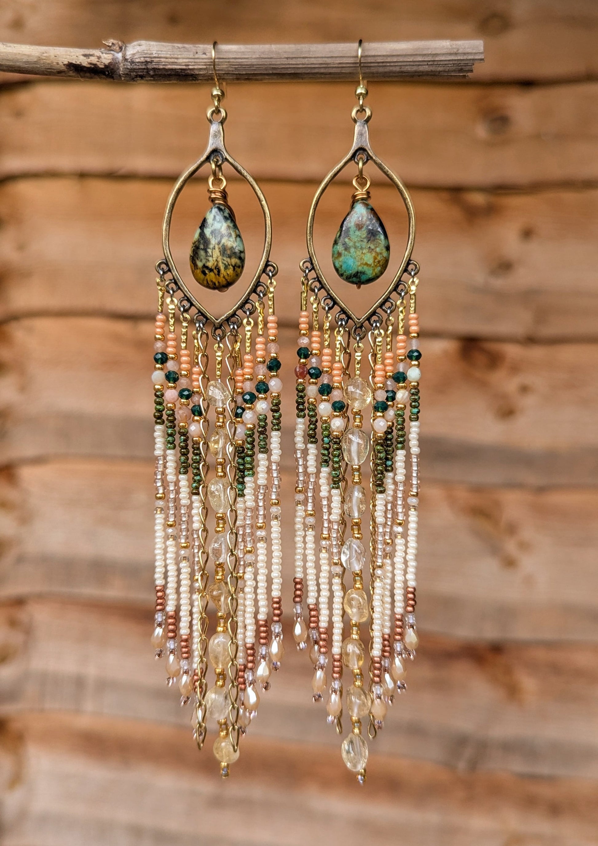 Delicate beaded earrings with teardrop-shaped gemstones on a wooden background