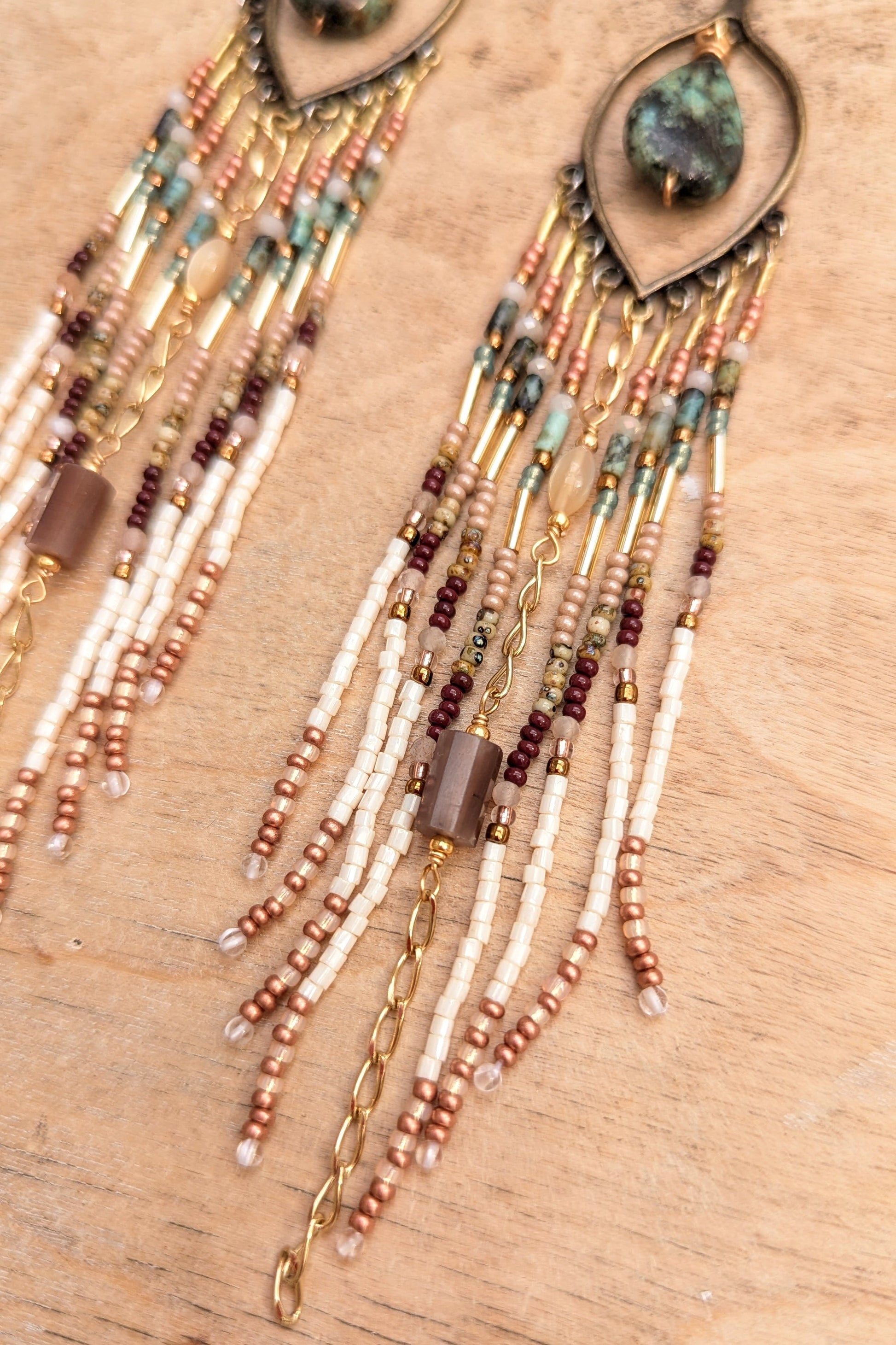 Beaded earrings with gold and multicolored beads on a wooden surface.