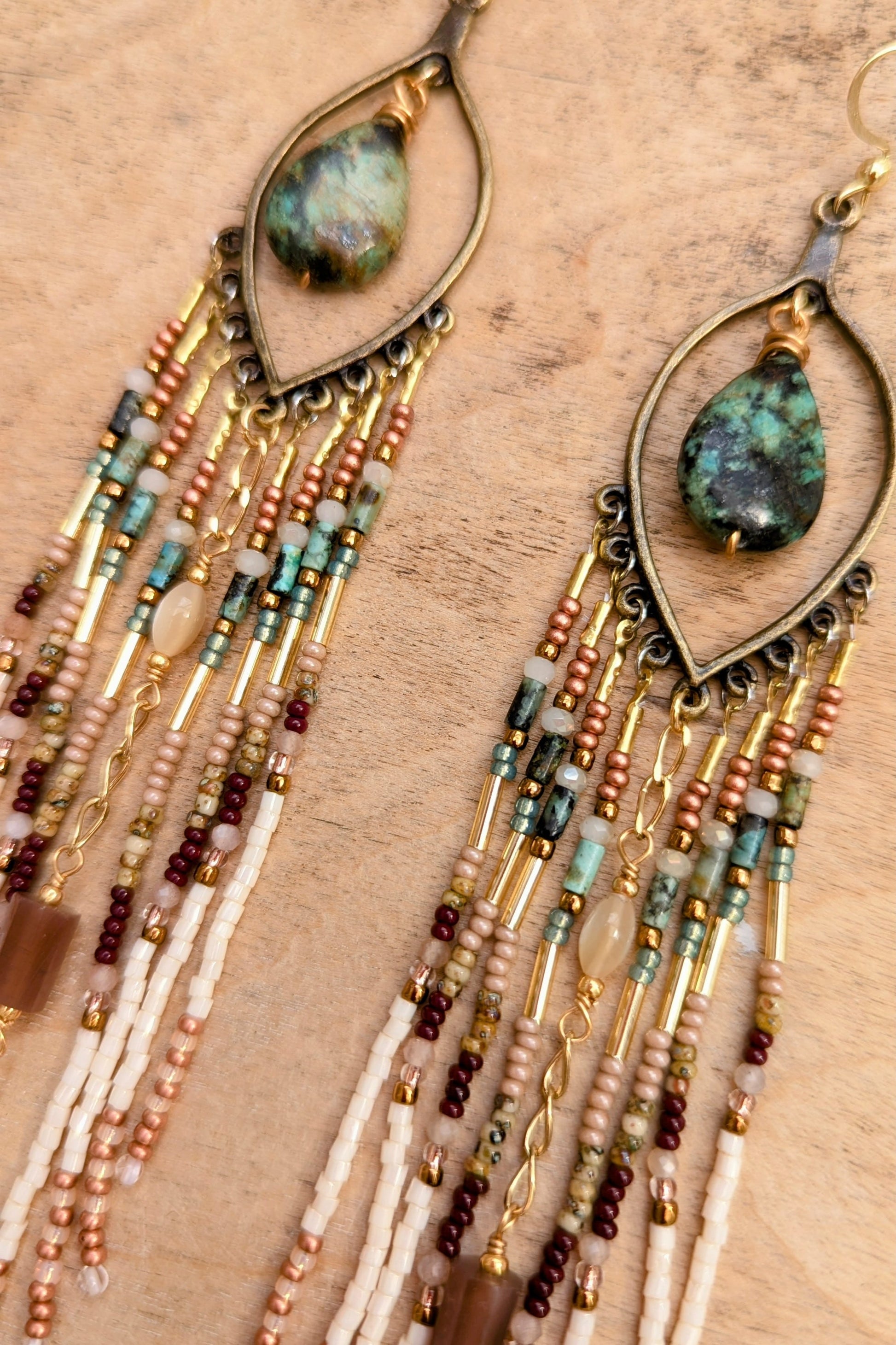 Beaded earrings with teardrop-shaped stones on a wooden surface.