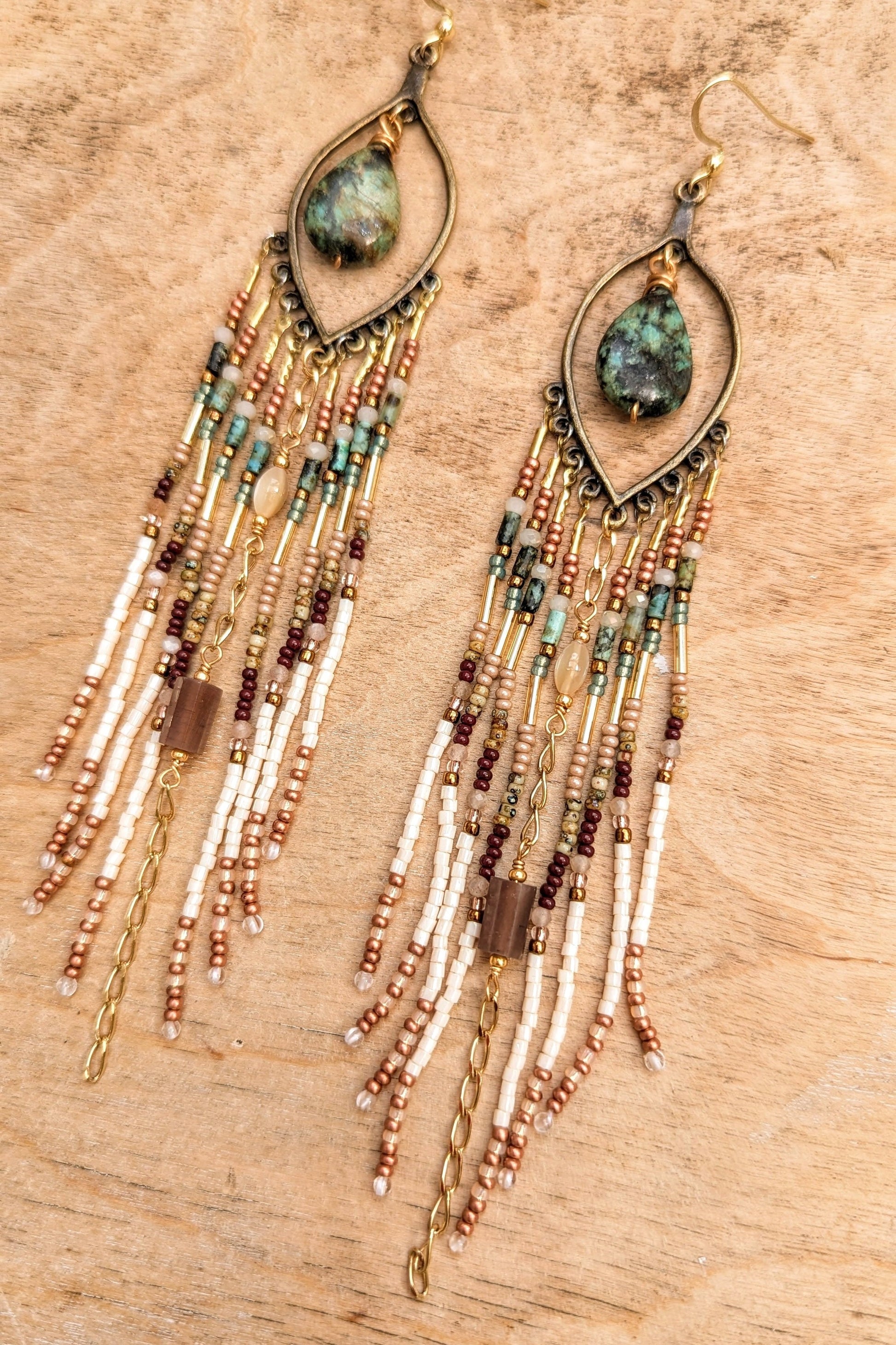 Beaded earrings with teardrop-shaped gemstones on a wooden surface by Moon & Milk.