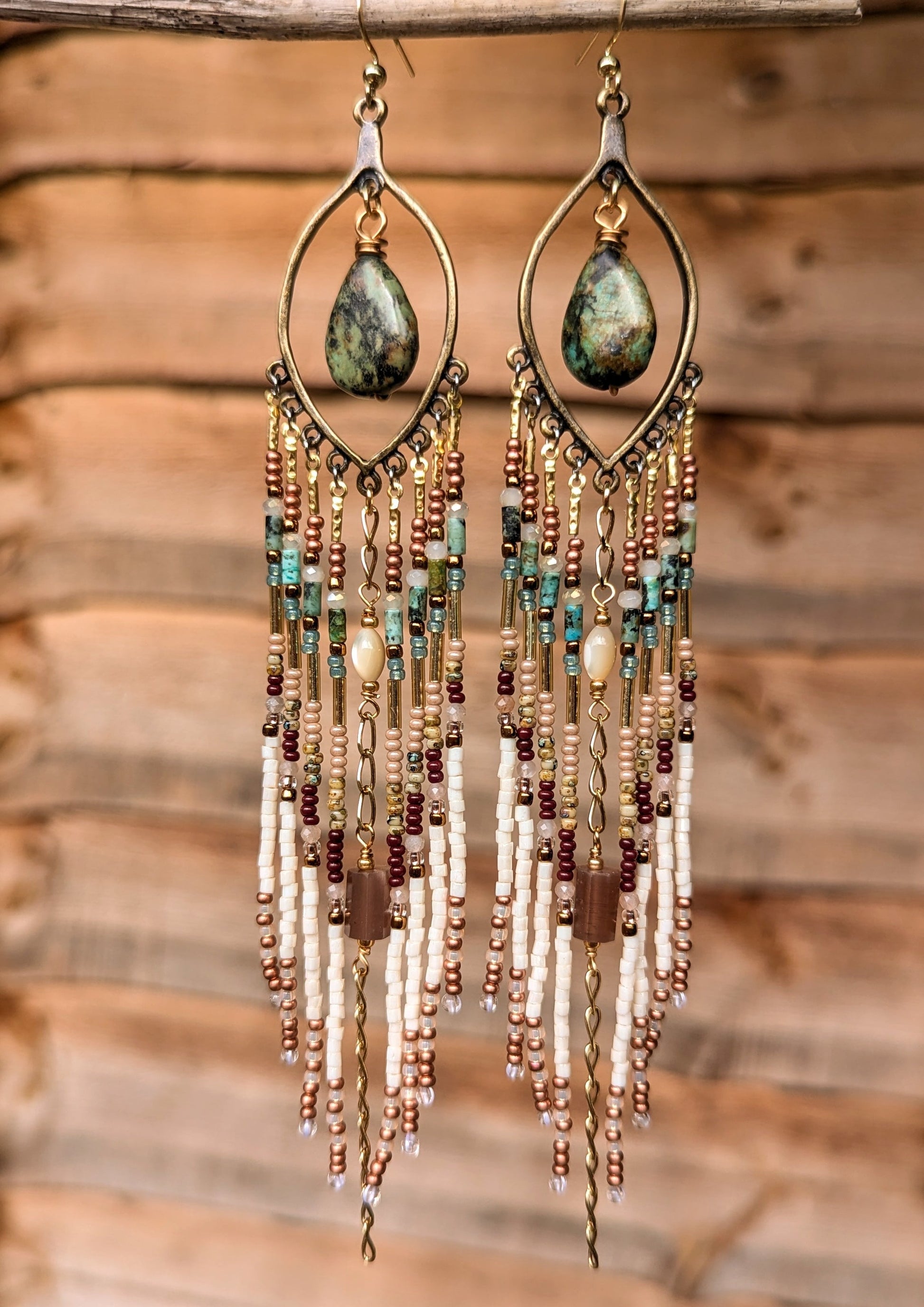 Delicate beaded earrings with teardrop-shaped turquoise stones hanging against a wooden background.