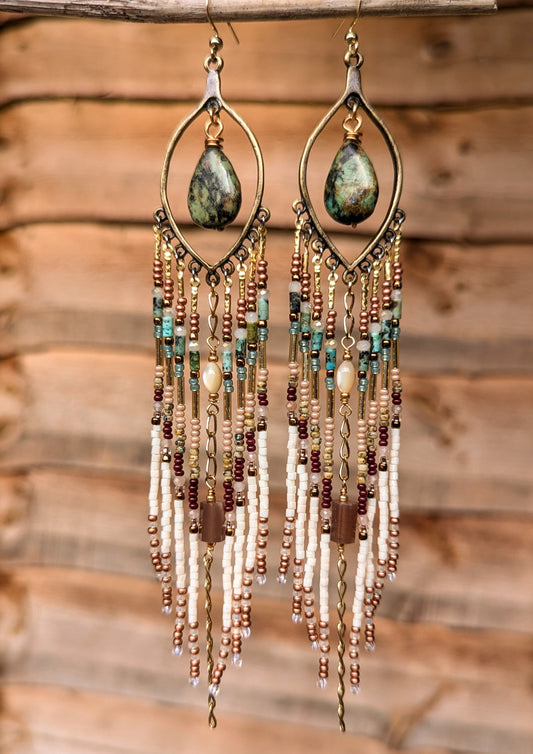 Delicate beaded earrings with teardrop-shaped turquoise stones hanging against a wooden background.