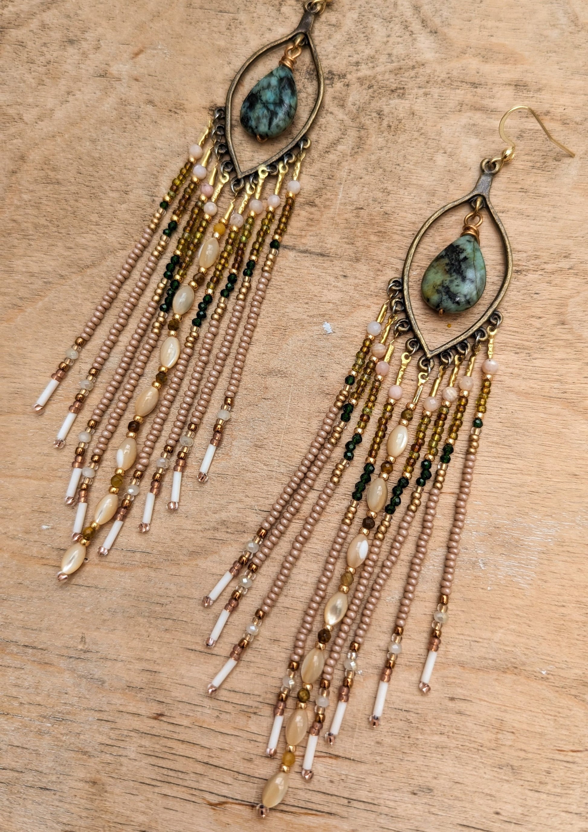 Long beaded earrings with teardrop-shaped gemstones on a wooden surface.