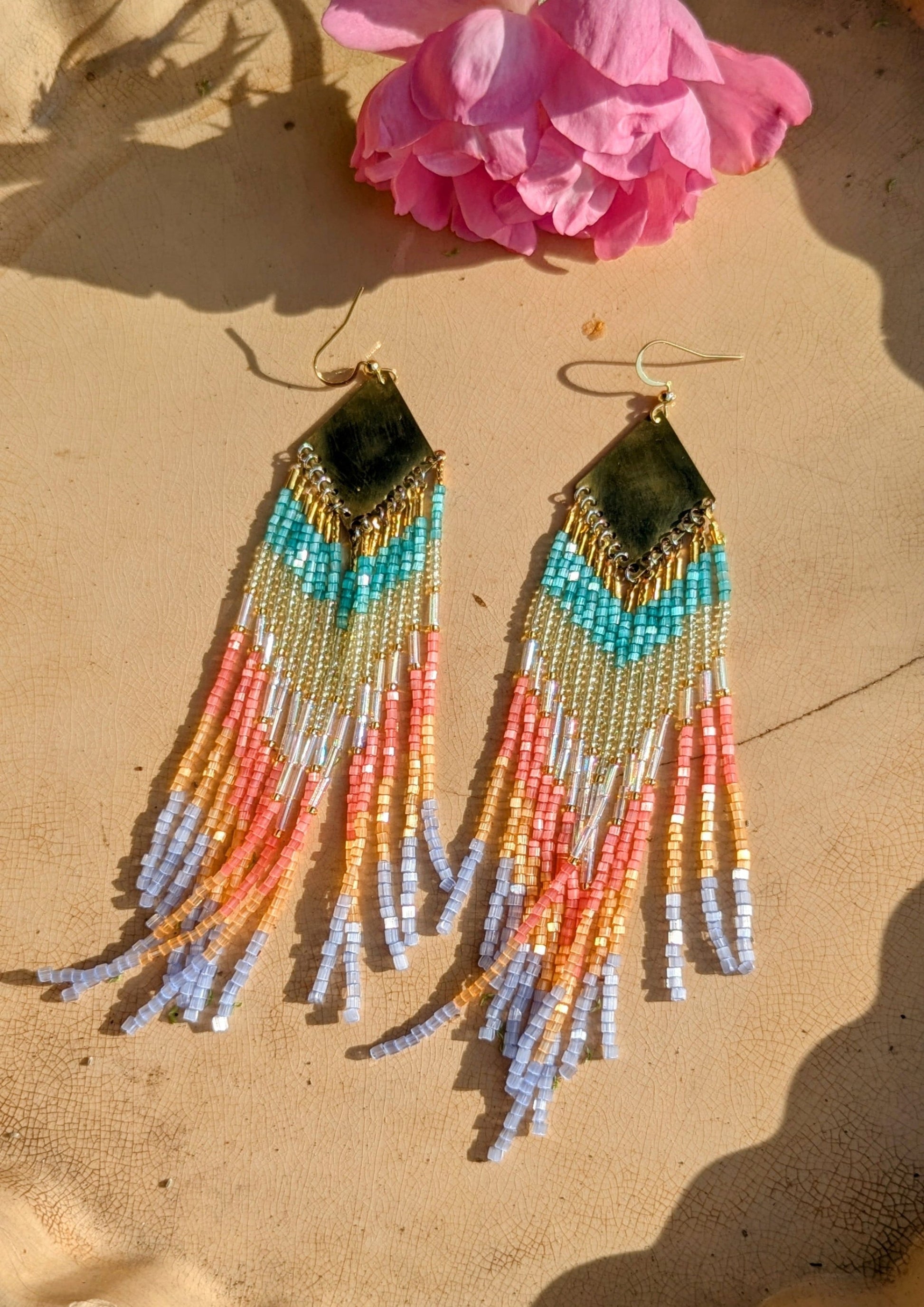 Multicolored handcrafted beaded earrings on a textured surface with a pink flower.