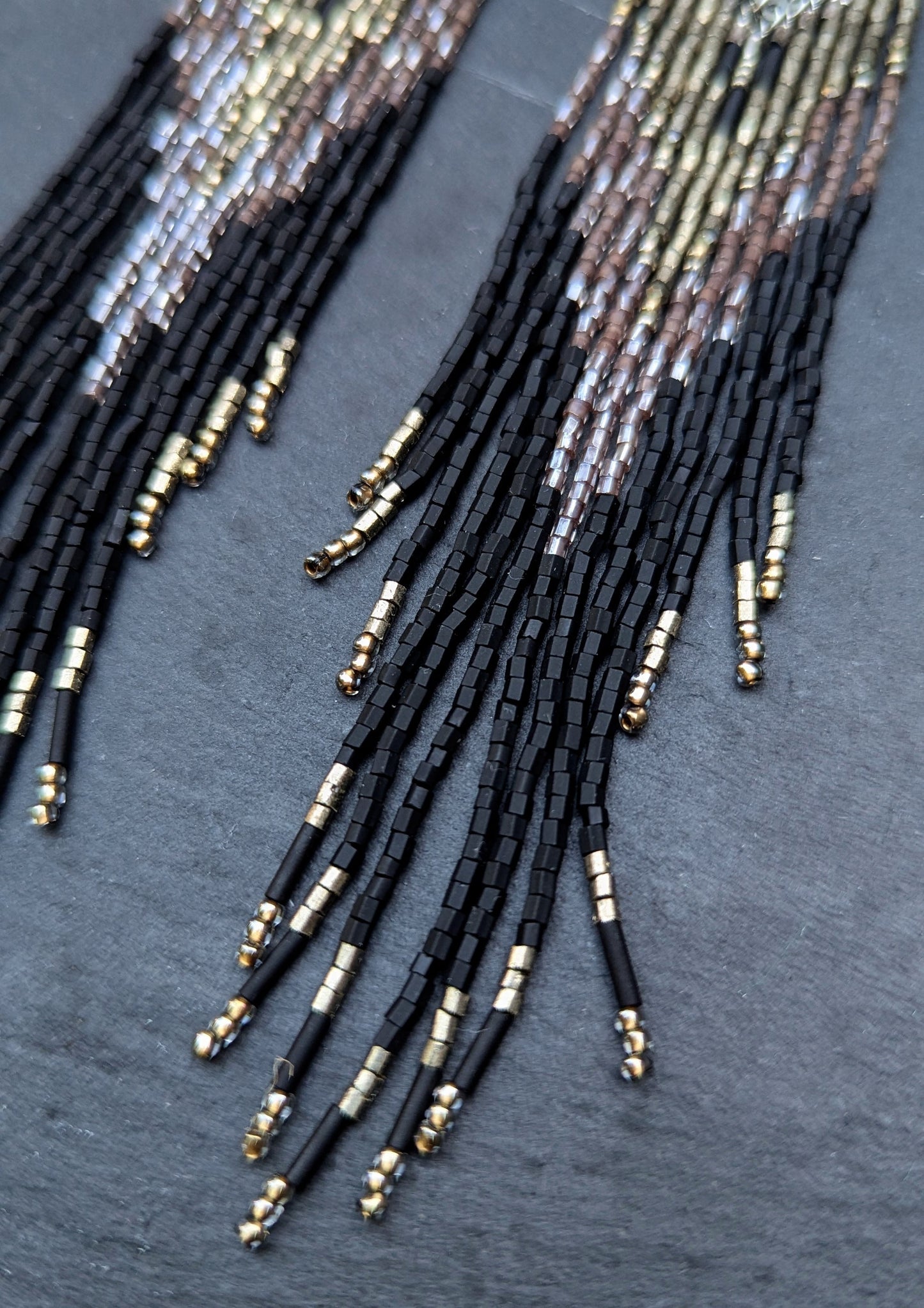 Close-up of beaded fringe earrings on a dark fabric background.