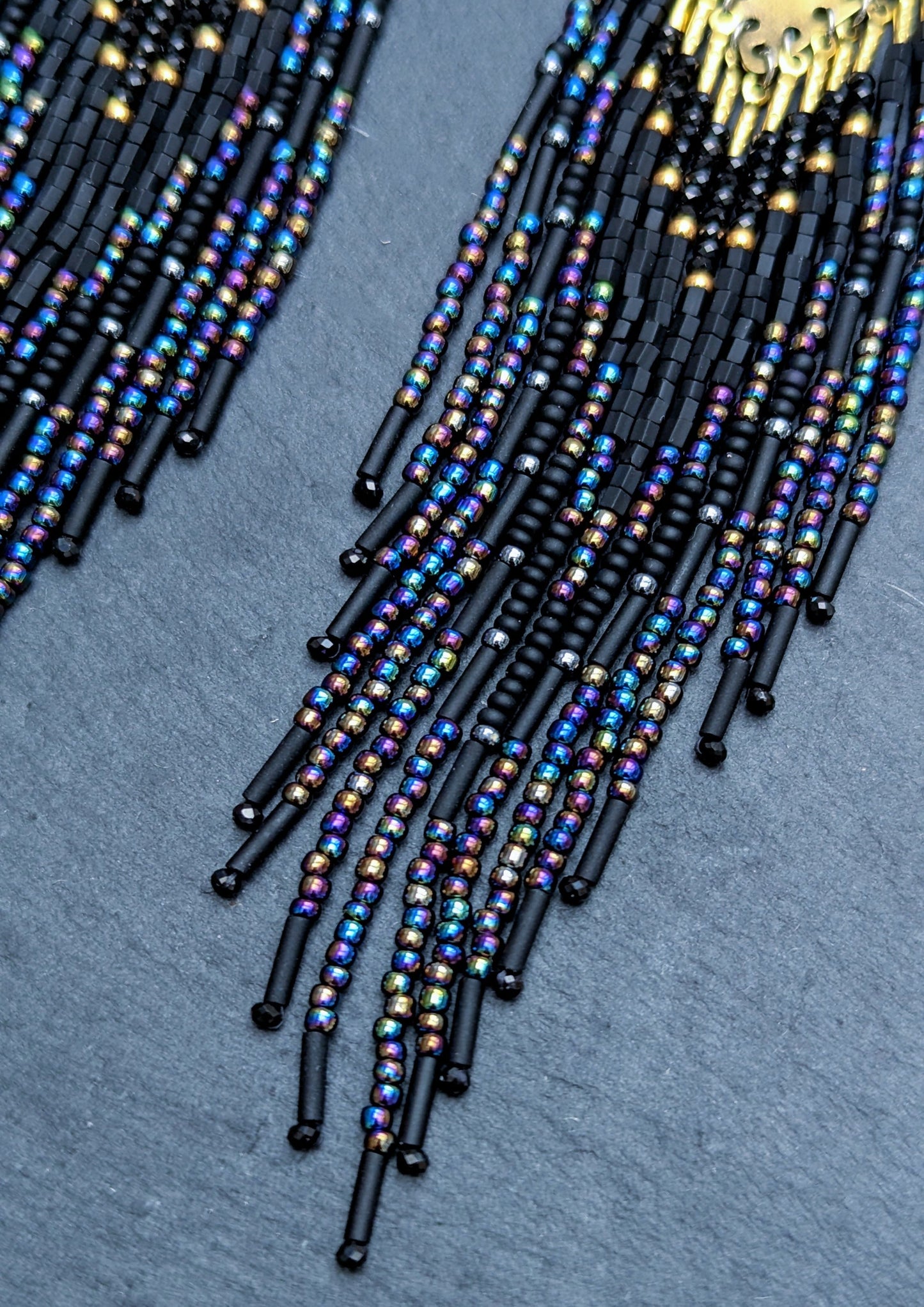 Close-up of black beaded fringe earrings on a gray background.