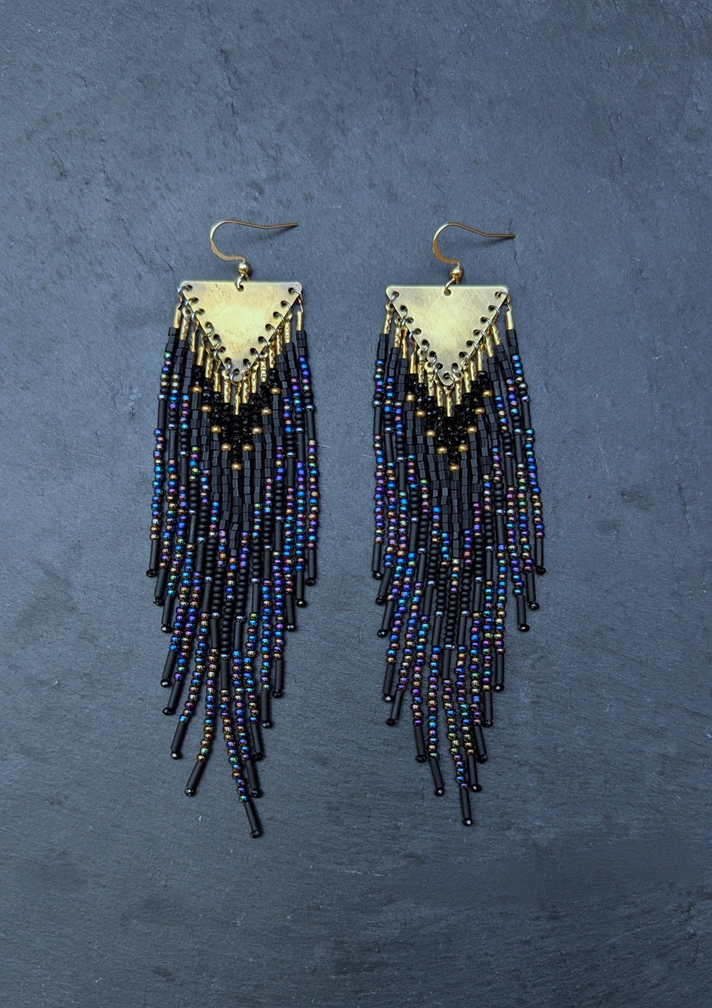 Pair of black beaded fringe earrings on a textured blue background by Moon & Milk.