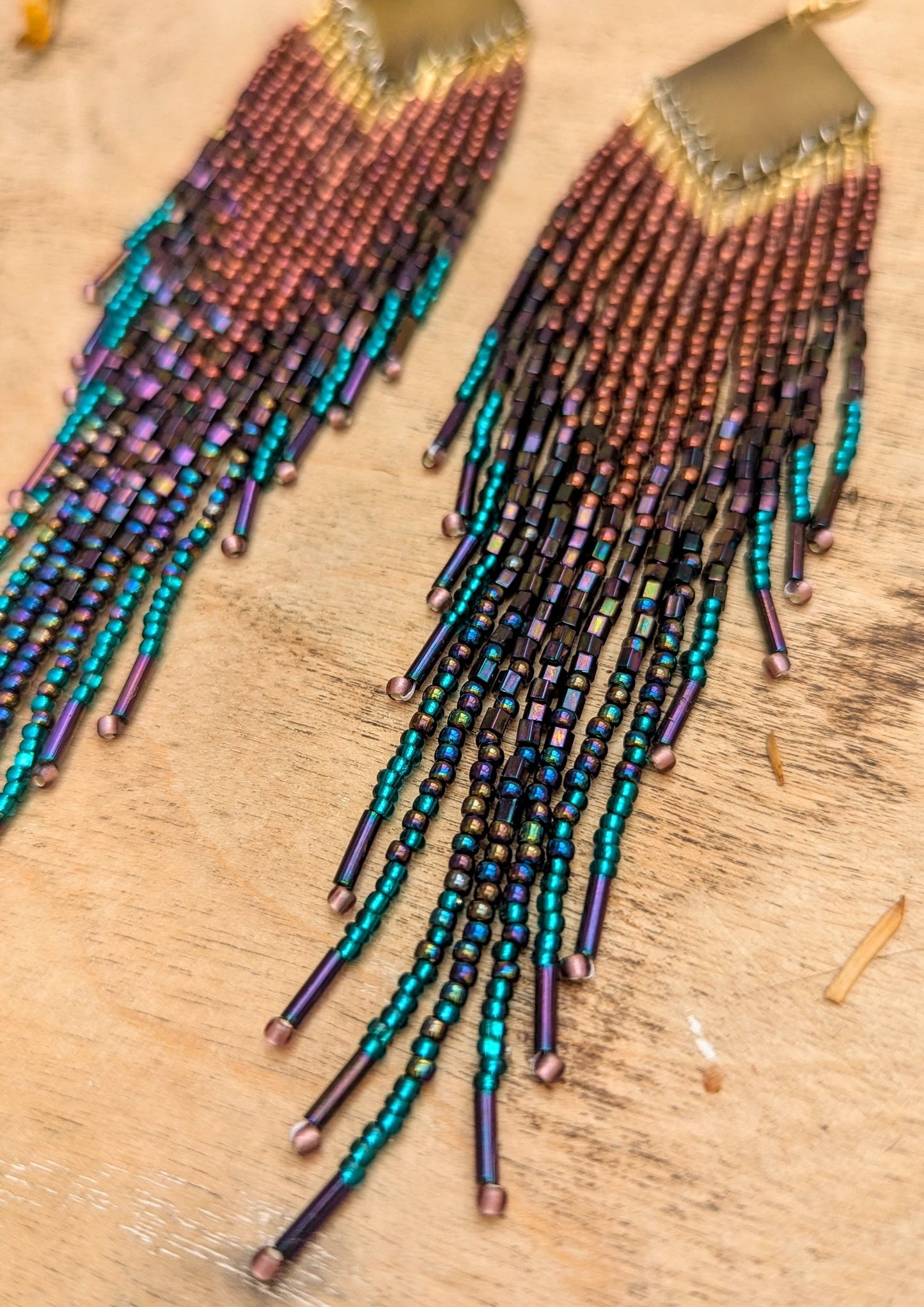 Hand beaded earrings with colorful fringe on a wooden surface by Moon & Milk.