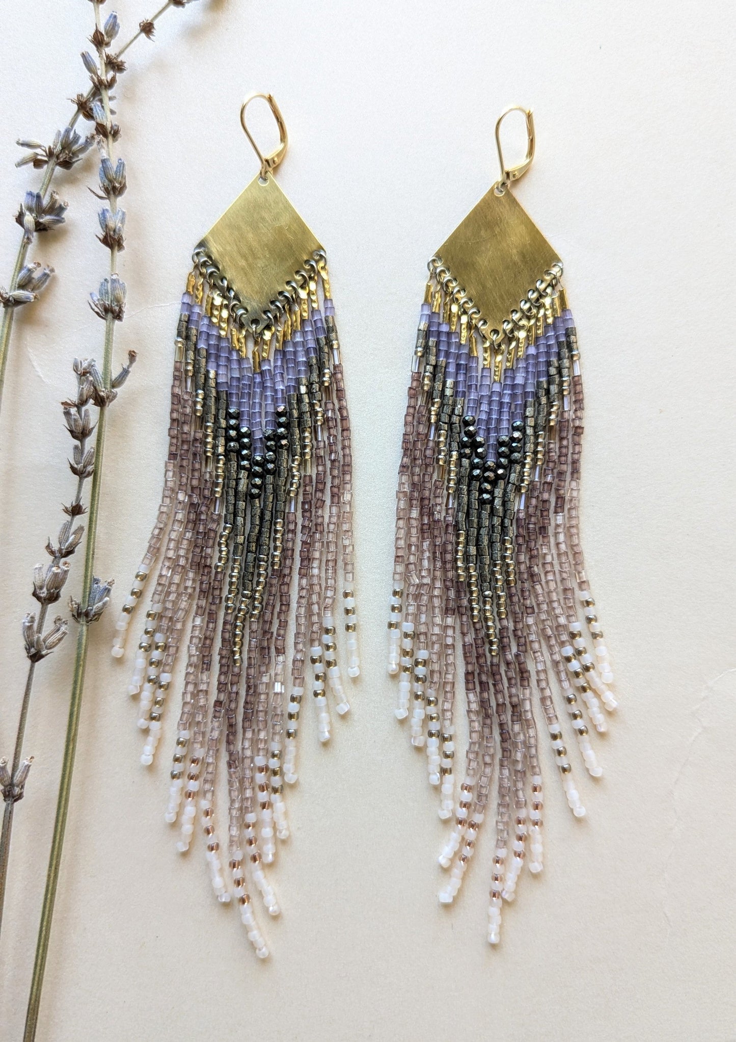 Long beaded earrings with metallic accents on a neutral background.