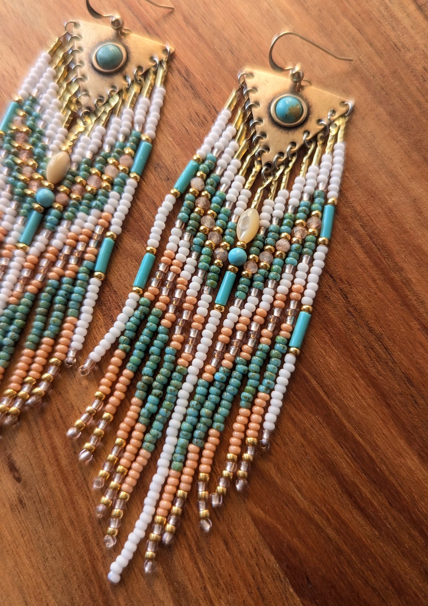 Pair of handcrafted beaded earrings with turquoise, gold, and white beads on a wooden surface by Moon & Milk.