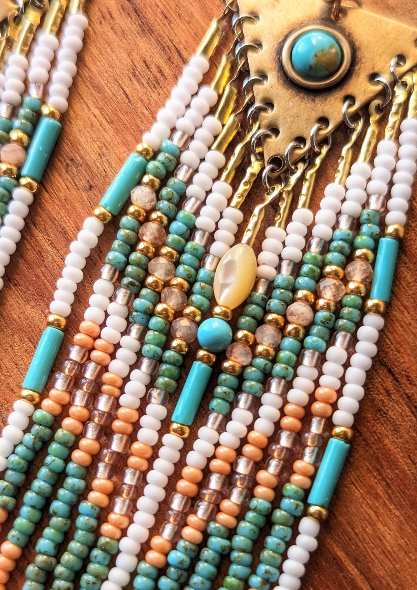 Close-up of handcrafted beaded earrings with turquoise, white, and gold beads on a wooden surface.