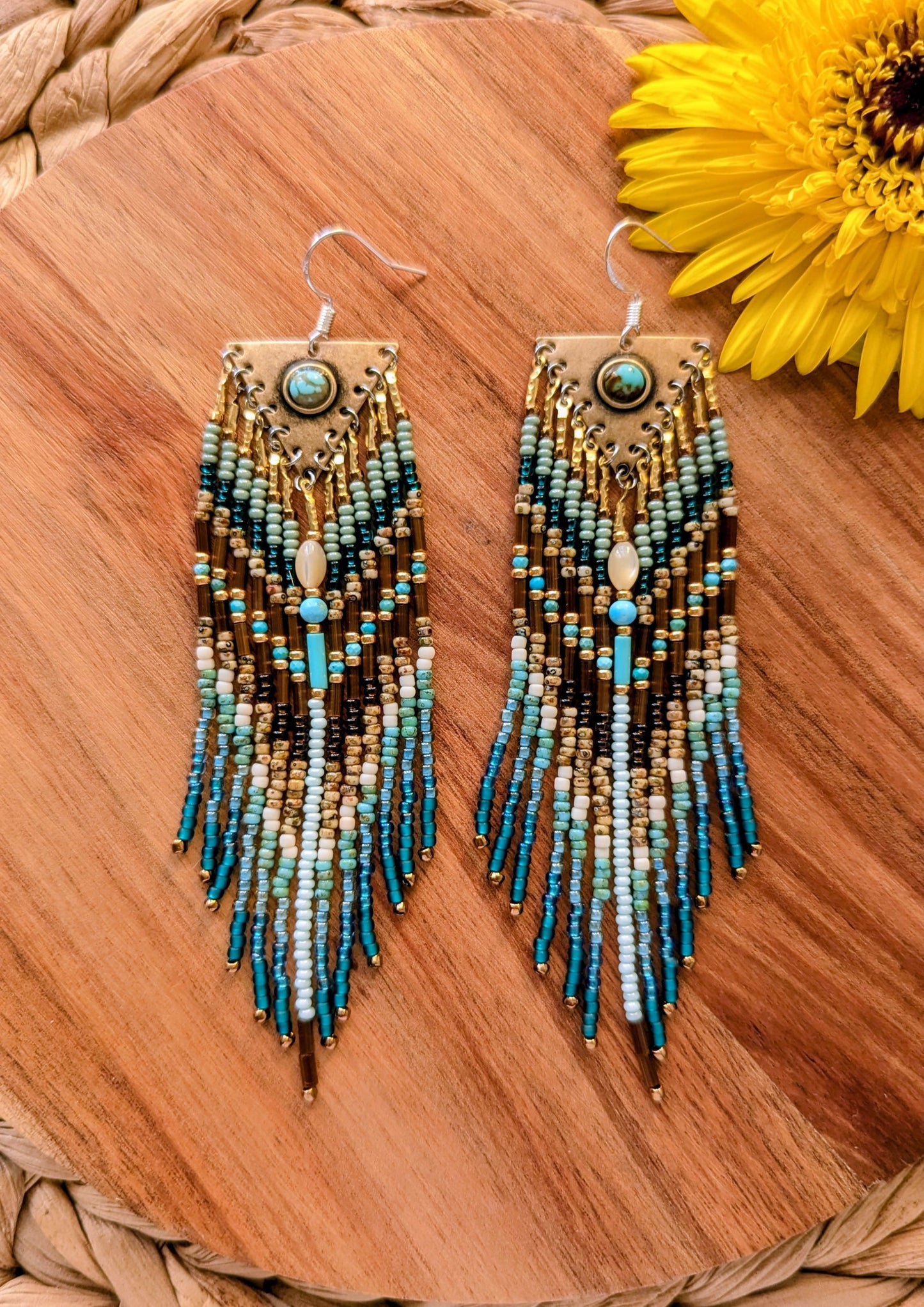 Beaded earrings with blue and green gradient on a wooden surface with a sunflower.