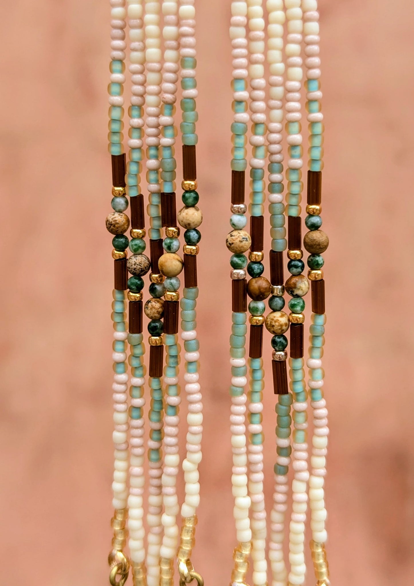 A close-up of beaded fringes with green, gold, and brown beads on a pink background.