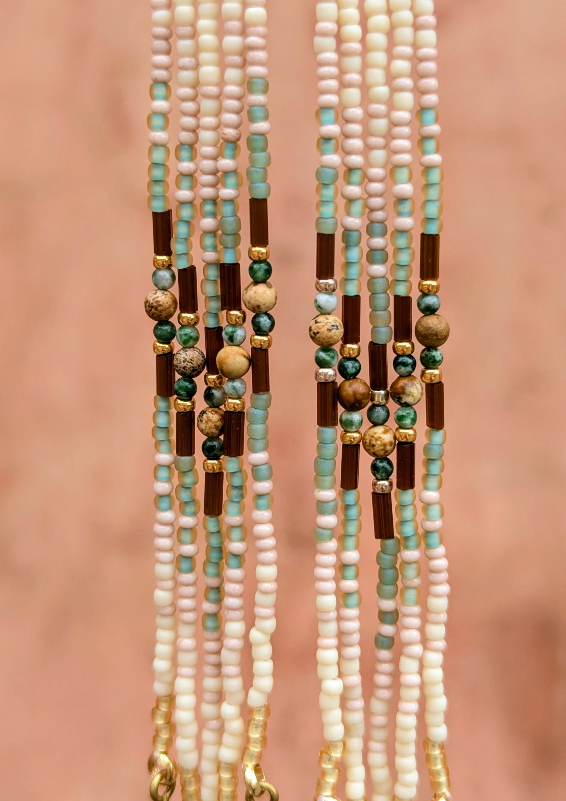 A close-up of beaded fringes with green, gold, and brown beads on a pink background.