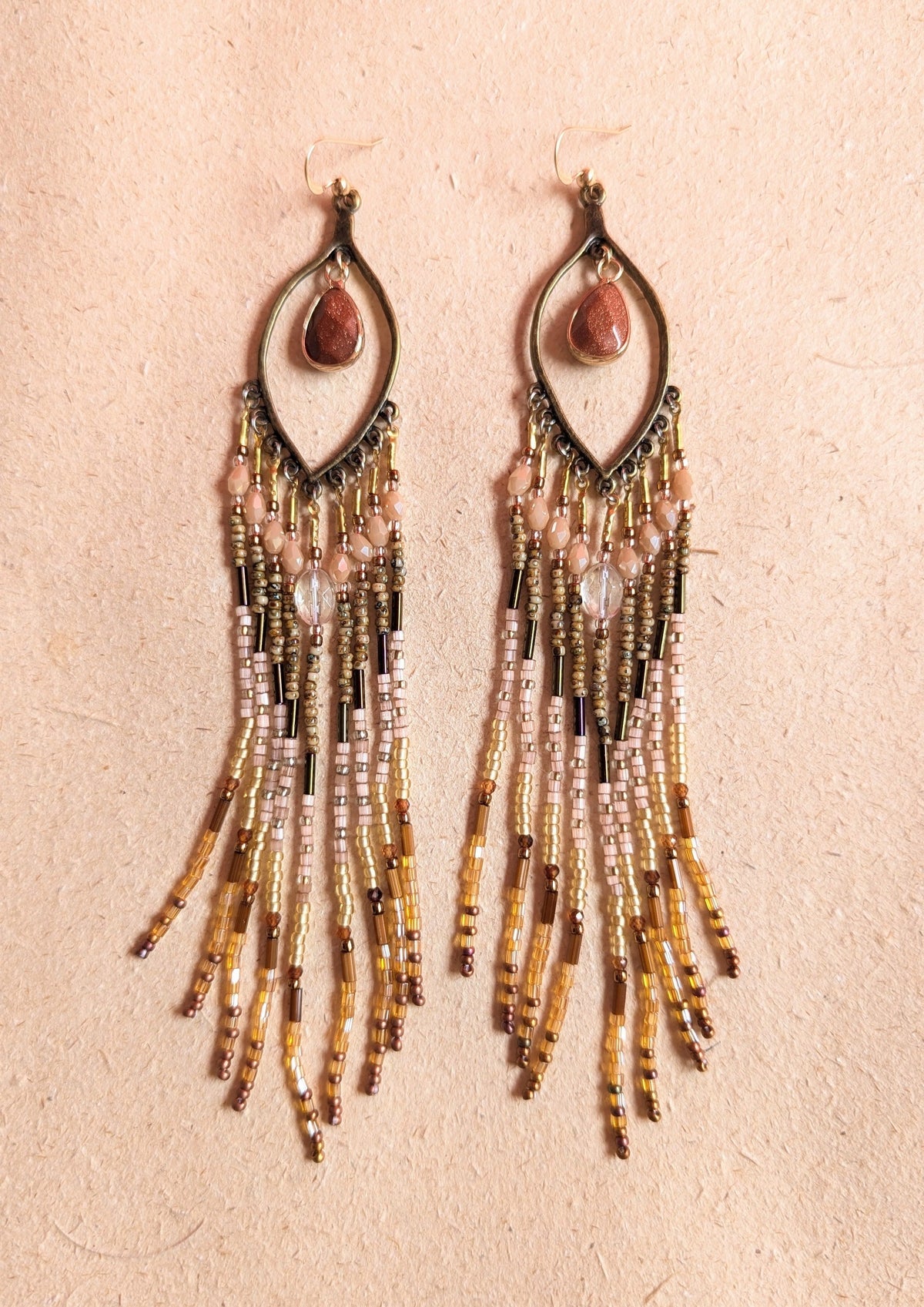 Boho beaded earrings with sanstones teardrops at the center on a beige background.