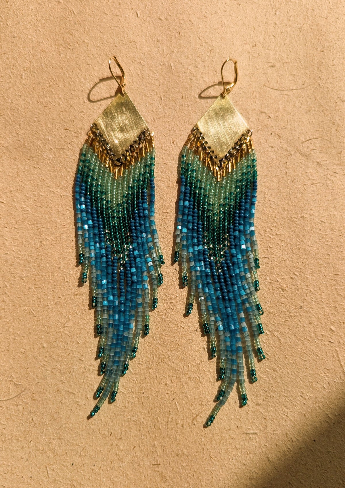 Pair of beaded earrings with blue and green gradient on a beige background.