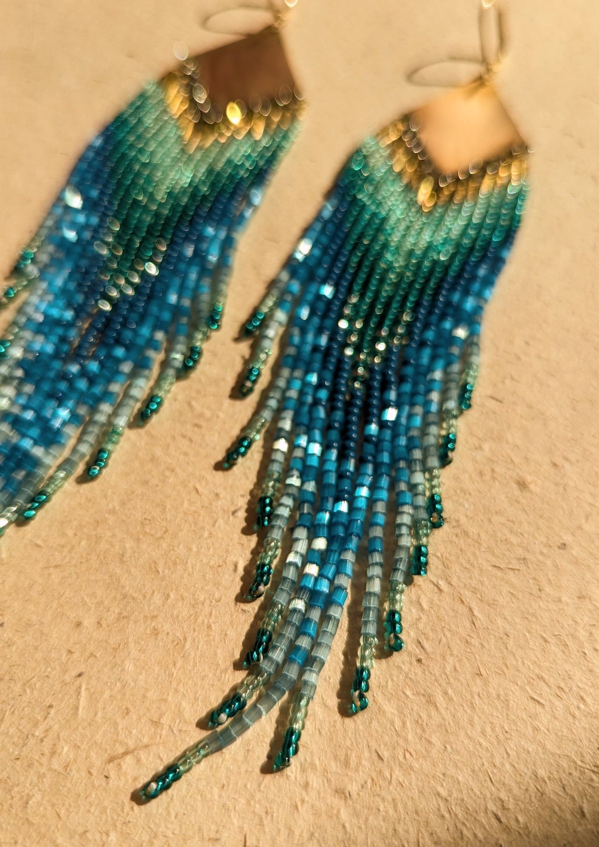 Sparkly blue ombre beaded earrings on a beige background.