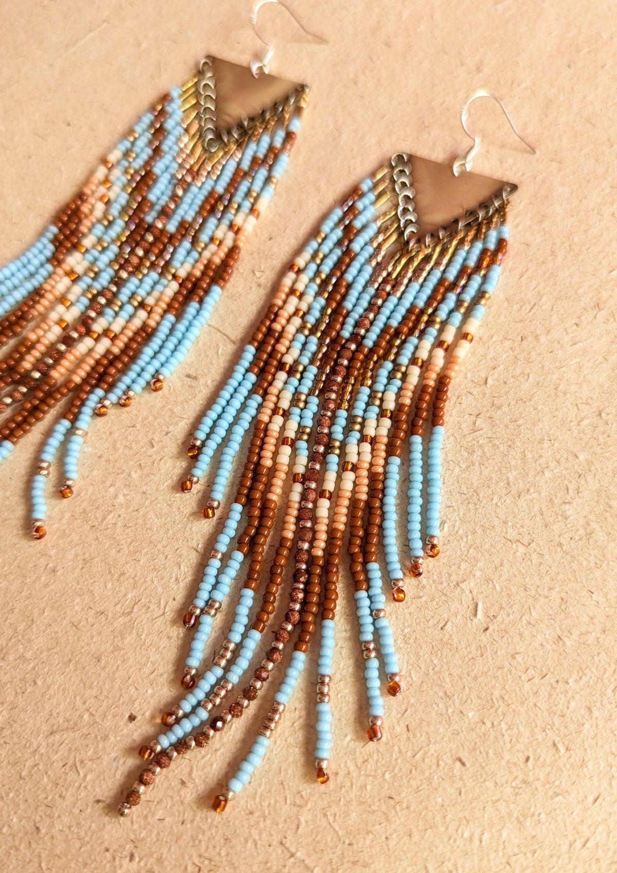 Beaded earrings with blue, terracotta, and burnt orange beads on a beige background.