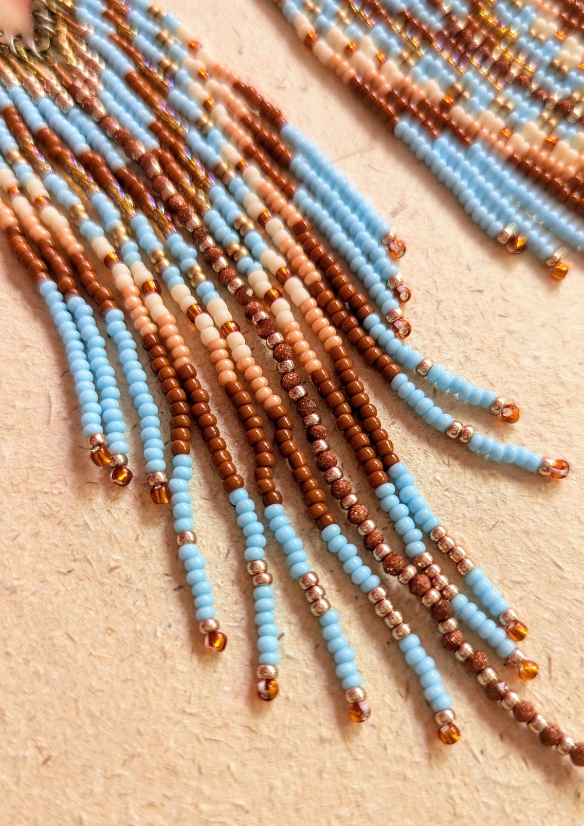 Beaded earrings in sky blue and terracotta on a beige surface.