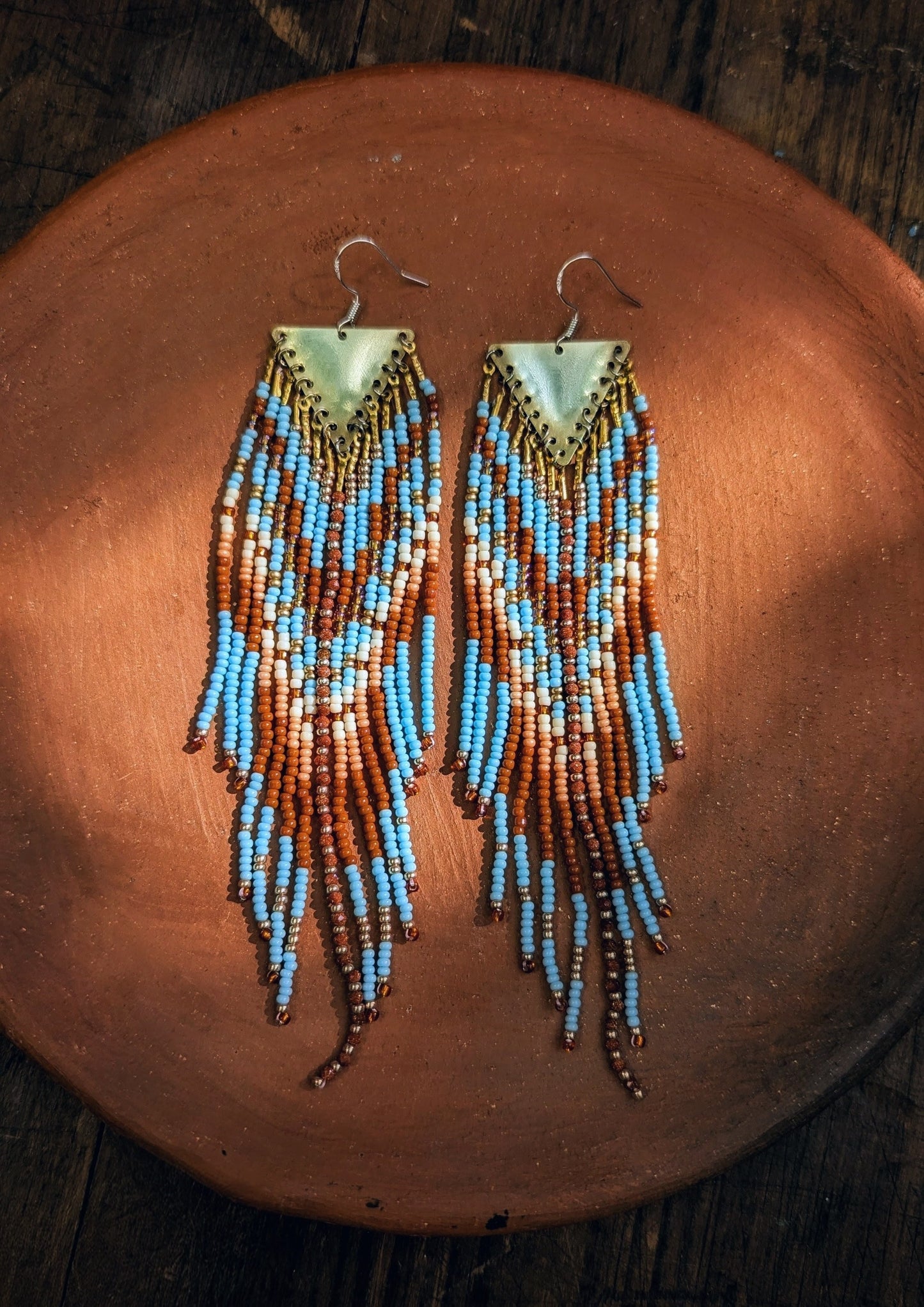 Pair of sky blue beaded earrings on a terracotta plate and wooden surface.