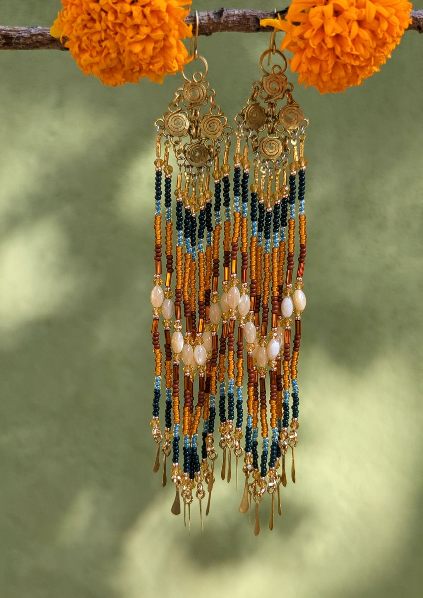 Brass earrings with seed beads on a branch with orange marigold flowers.
