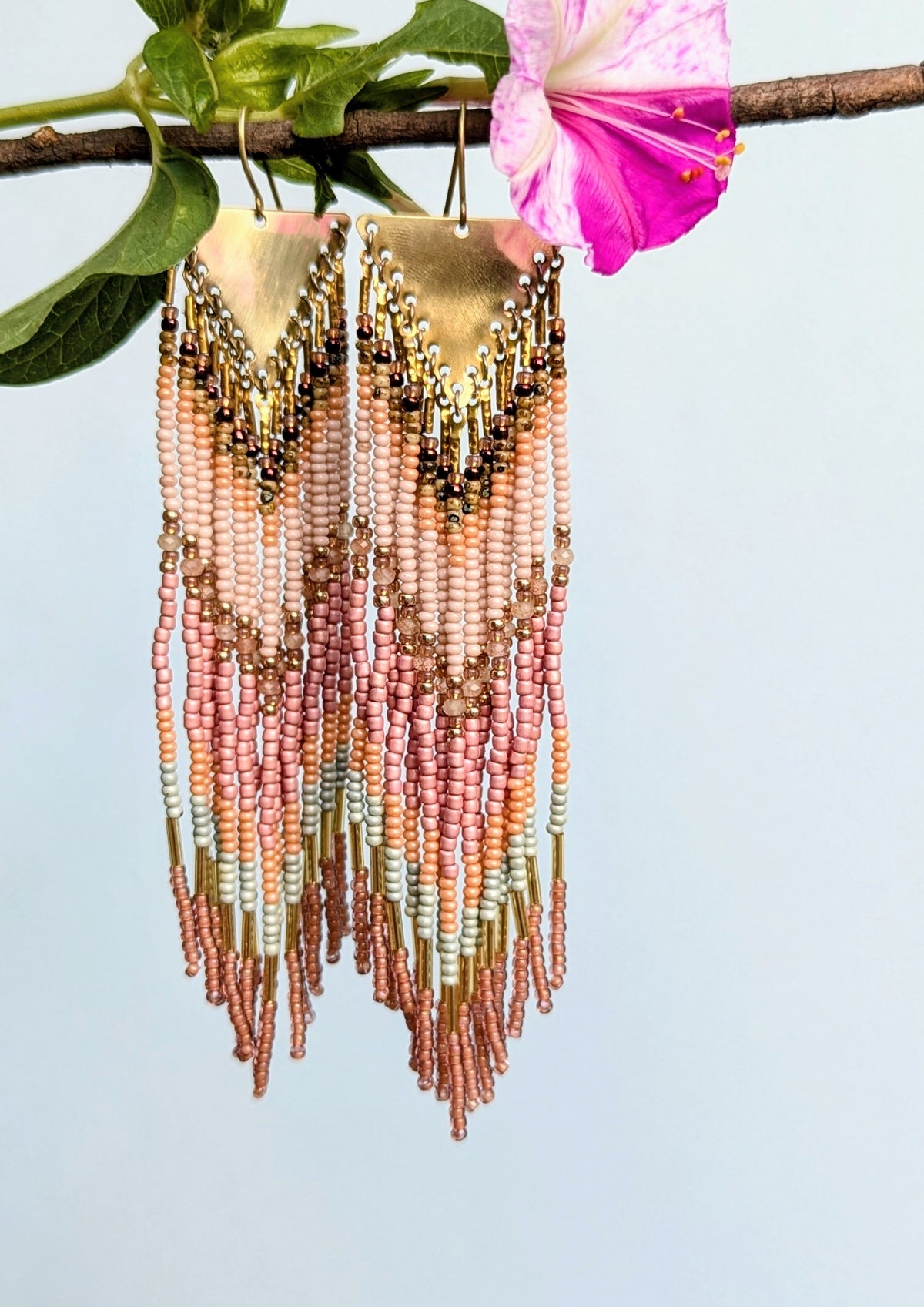 Beaded earrings with gold and pink accents against a light blue background.