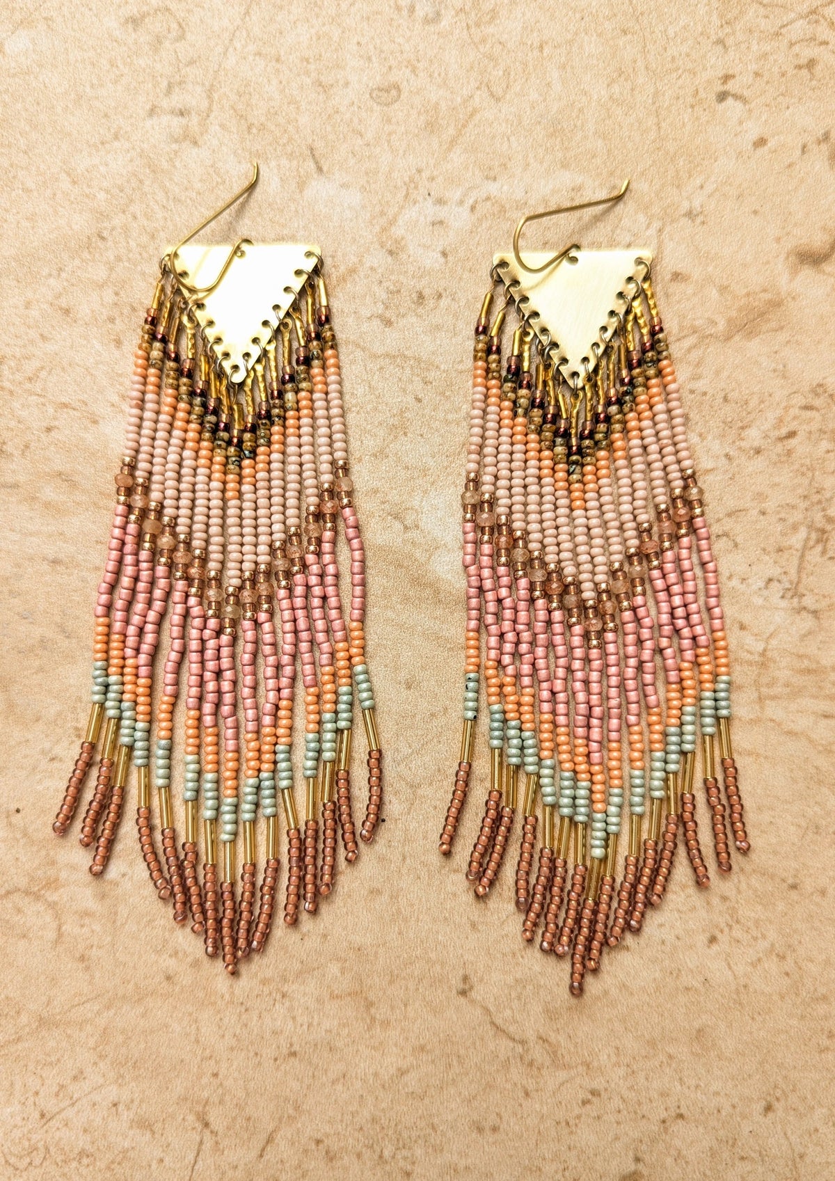 Beaded pink earrings with gold triangle tops on a beige background.