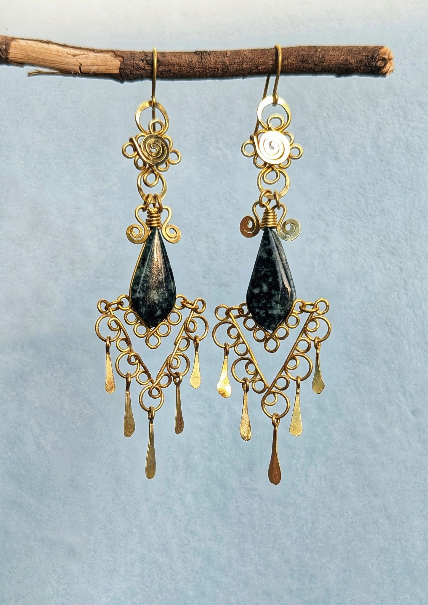 Brass and jade teardrop earrings hanging from a branch against a light blue background.