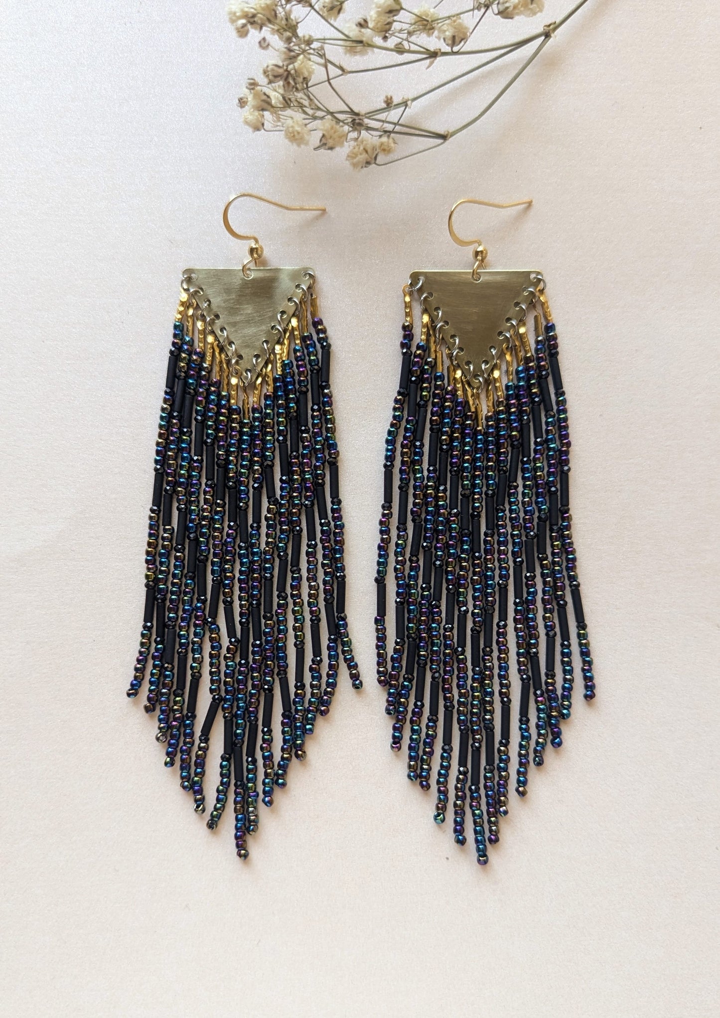 Pair of black iridescent beaded fringe earrings on a light background.