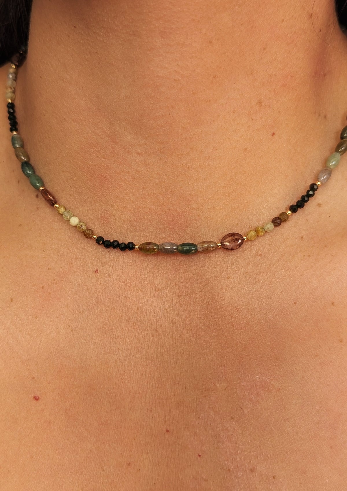 Close-up of a woman wearing a gemstone agate beaded necklace on a plain background.