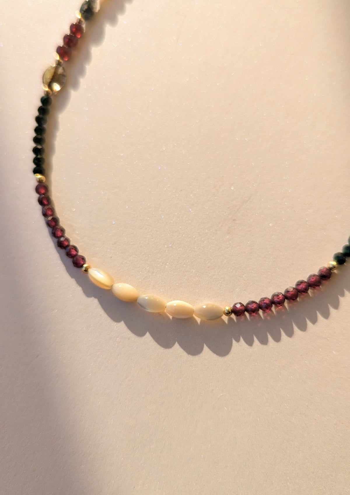 Necklace with gemstone and mother of pearl beads on a beige background.