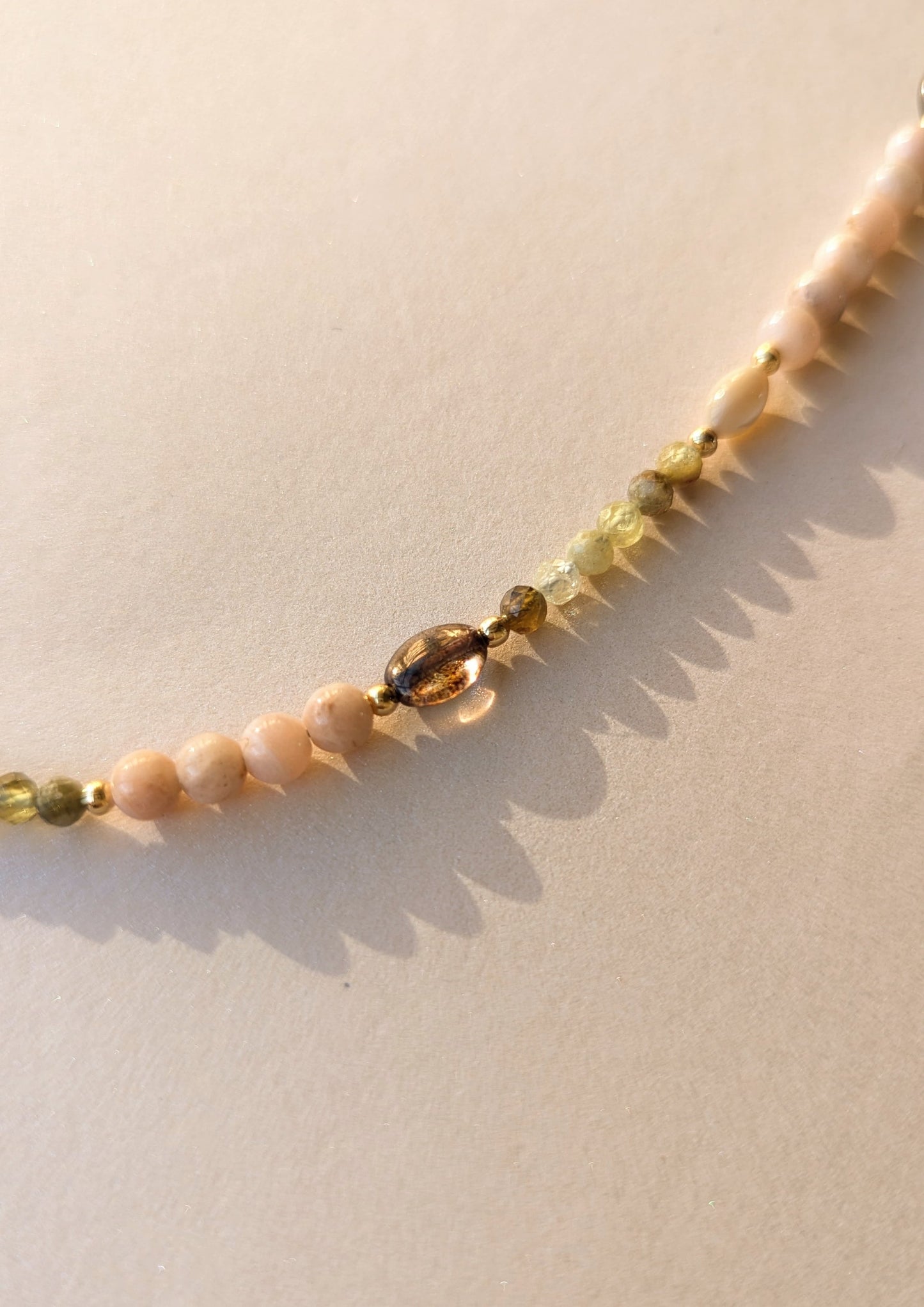 Necklace with moonstone, mother-of-pearl, and garnet beads on a light background.