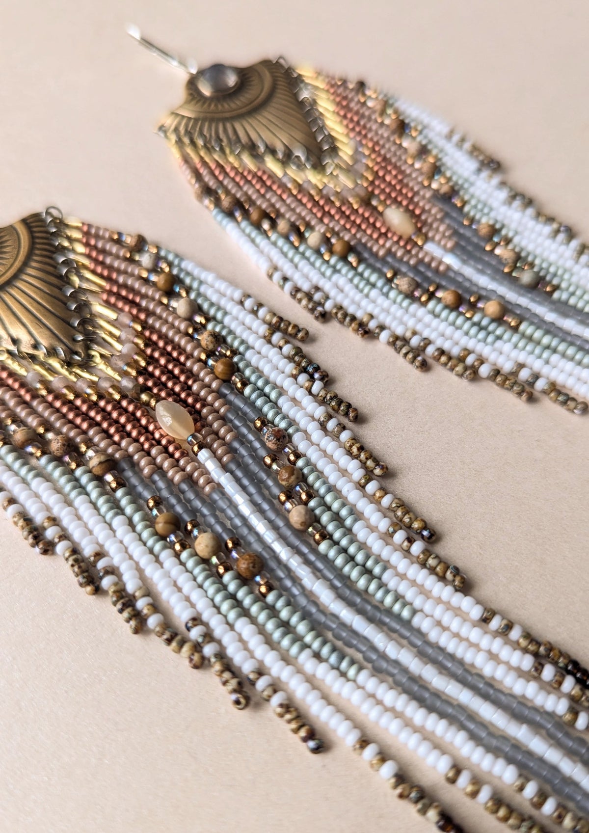 Beaded earrings with gold, silver, and bronze elements on a beige background
