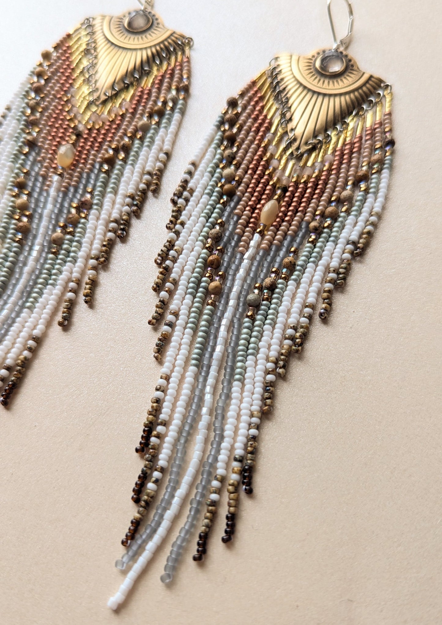 Long beaded earrings with gold accents on a beige background.