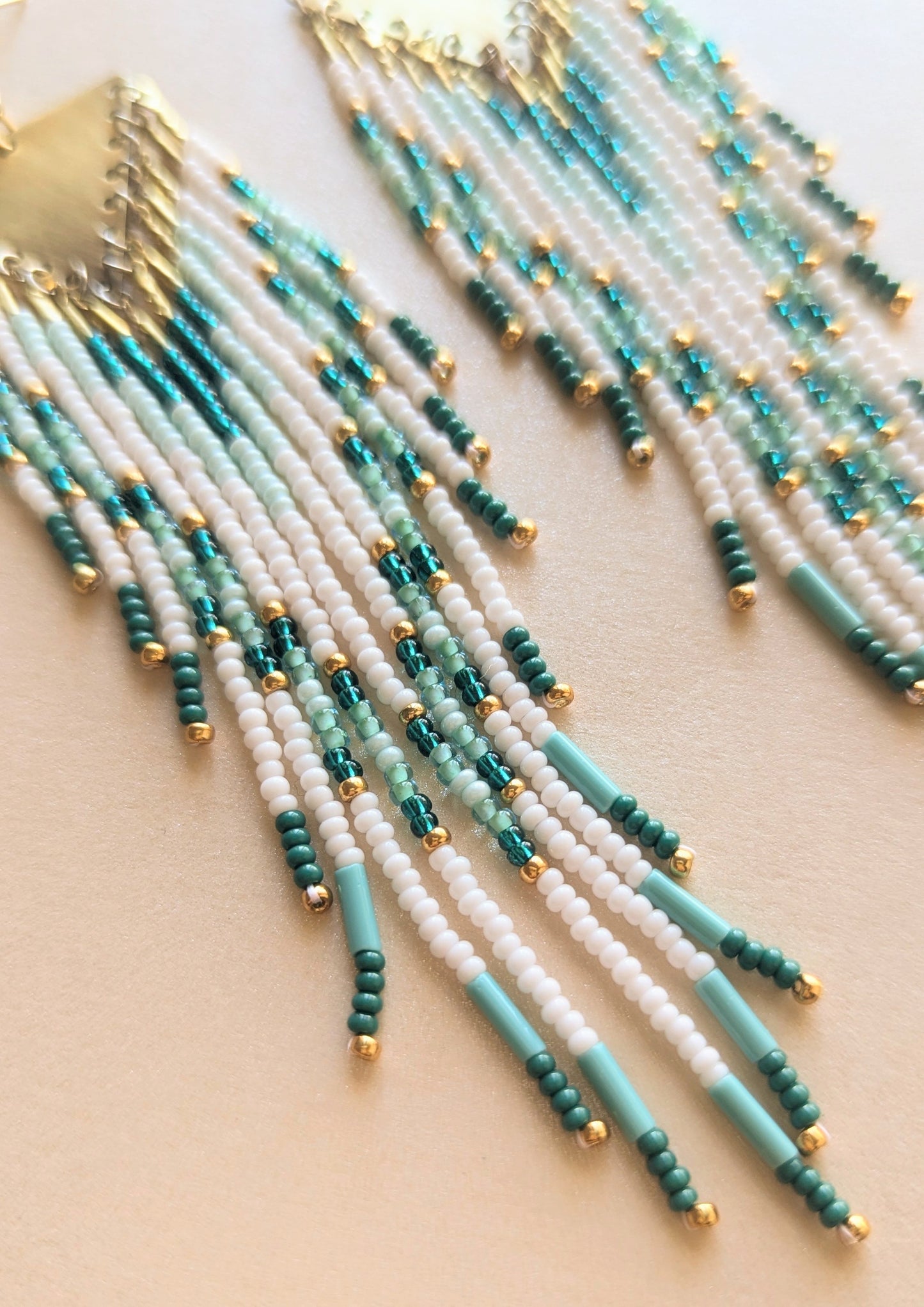Beaded earrings with turquoise, white, and gold beads on a beige background by Moon & Milk.