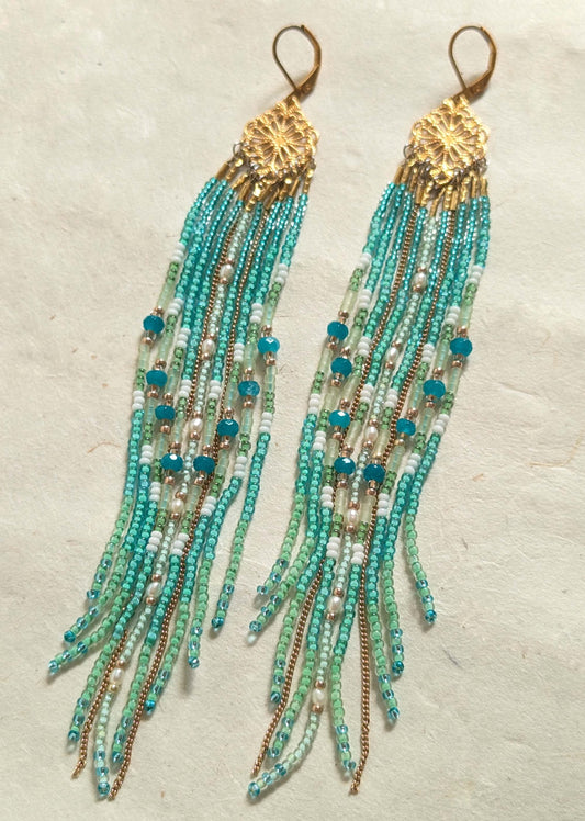 Turquoise beaded earrings with gold accents on a textured beige background by Moon & Milk.