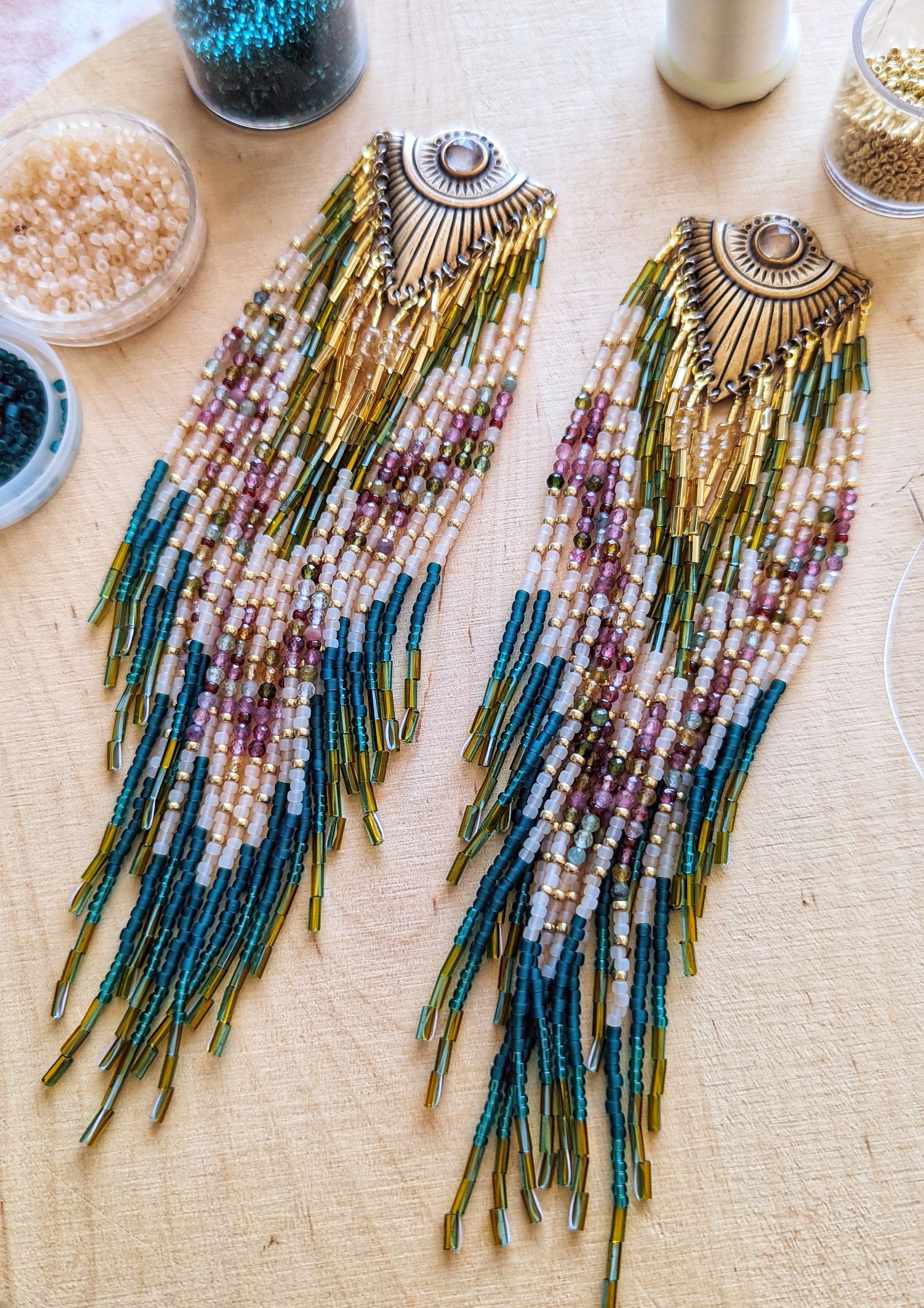 Handcrafted Moon & Milk beaded earrings honoring Xochipilli, with teal, gold, mauve, and watermelon tourmaline beadwork flowing from engraved brass fans.