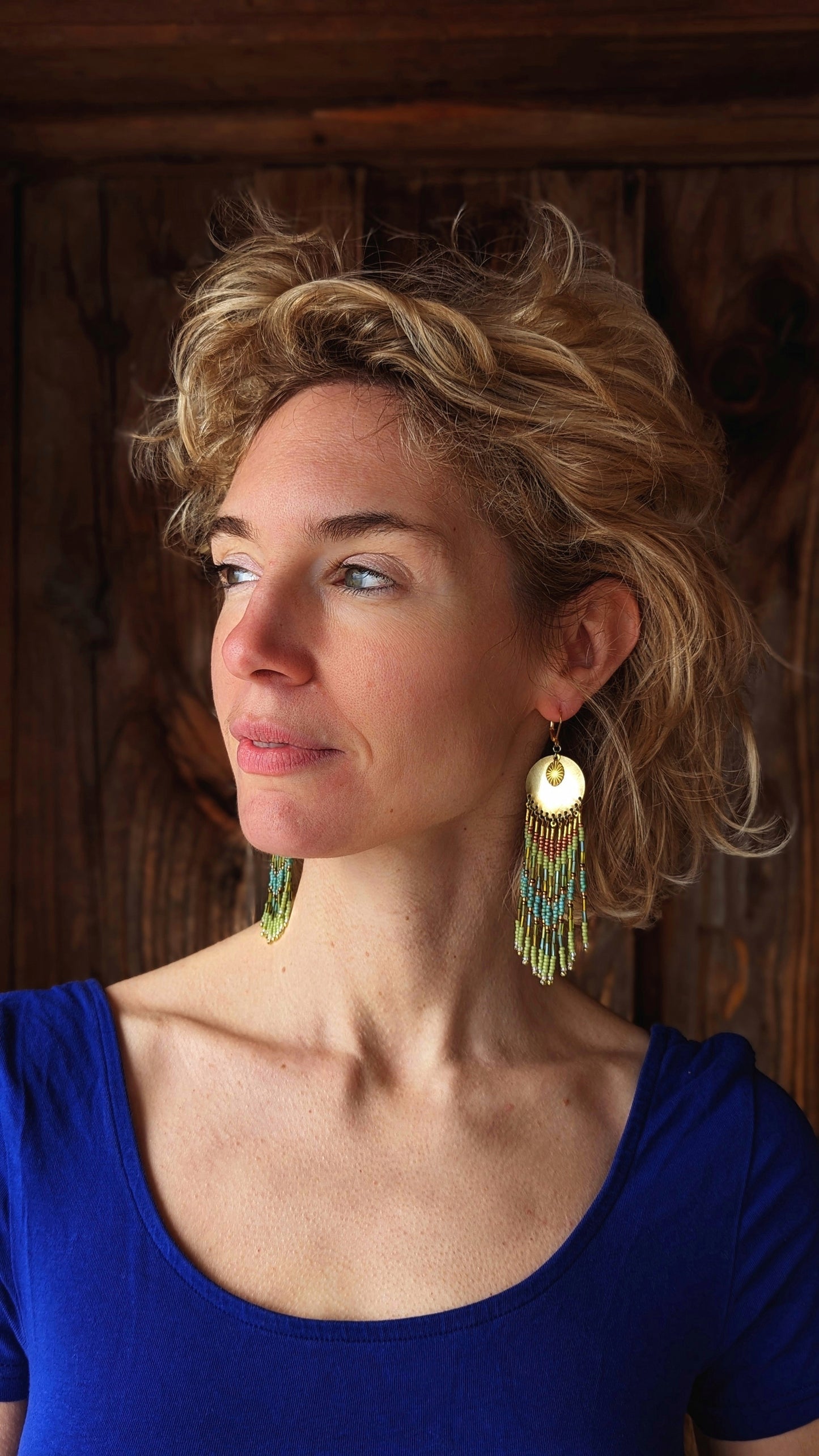 Moon & Milk handcrafted earrings with brass medallion, lime green, copper, and turquoise beaded fringe, worn by a woman.