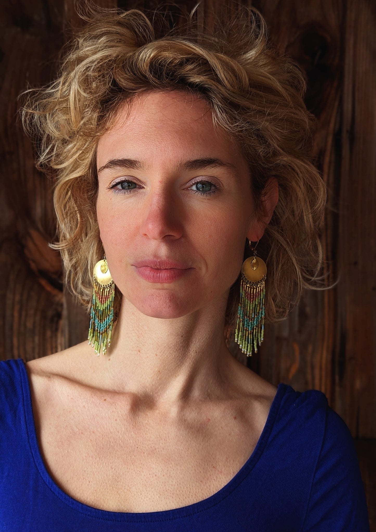 Moon & Milk handcrafted earrings with brass medallion, lime green, copper, and turquoise beaded fringe, worn by a woman.