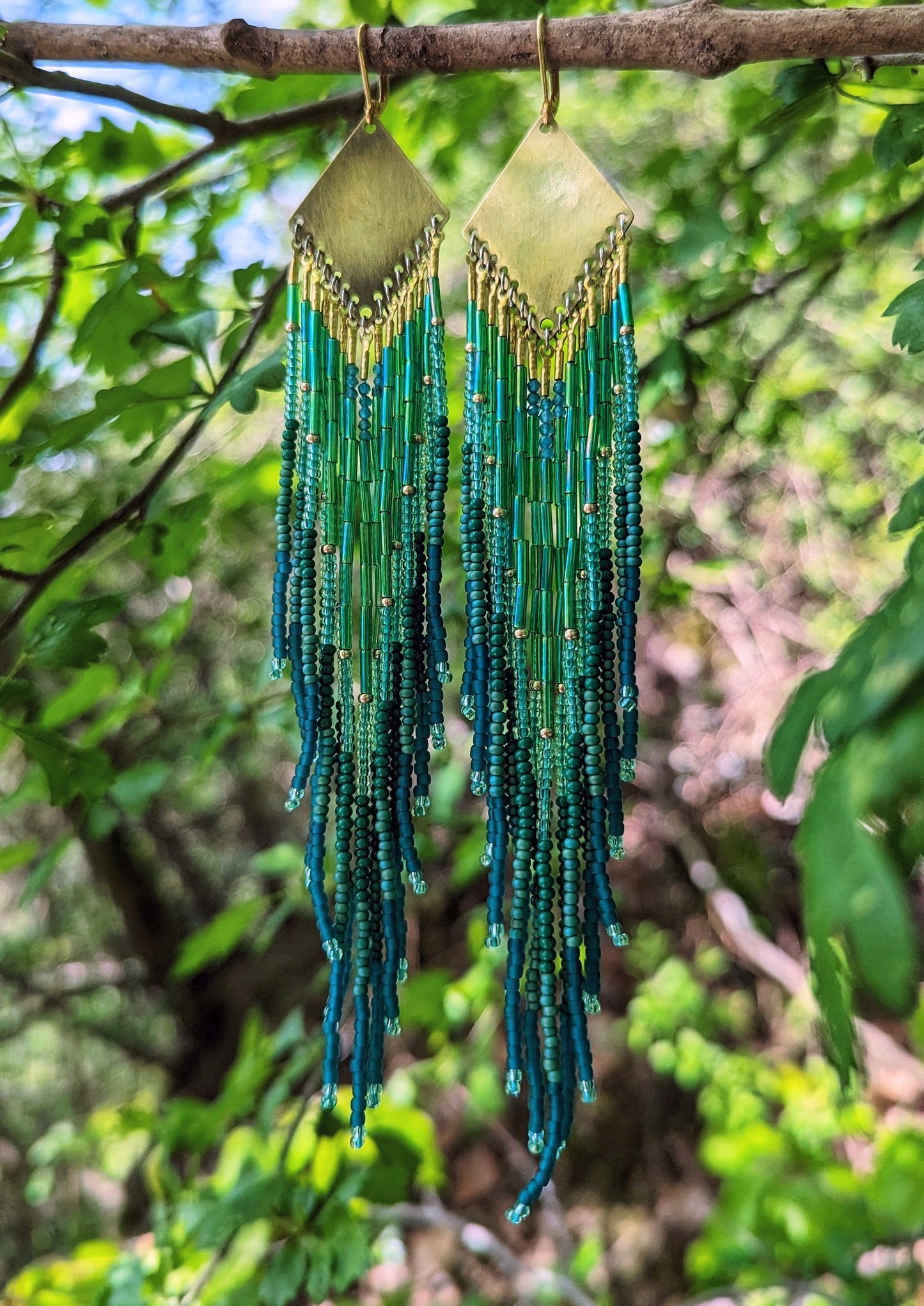 Long beaded earrings by Moon & Milk with deep green, teal, and blue fringe, brass diamond tops, and handcrafted detail inspired by the Swiss forest.