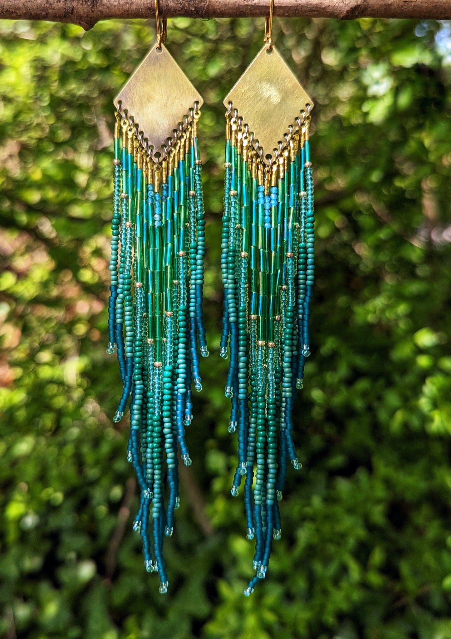 Long beaded earrings by Moon & Milk with deep green, teal, and blue fringe, brass diamond tops, and handcrafted detail inspired by the Swiss forest.