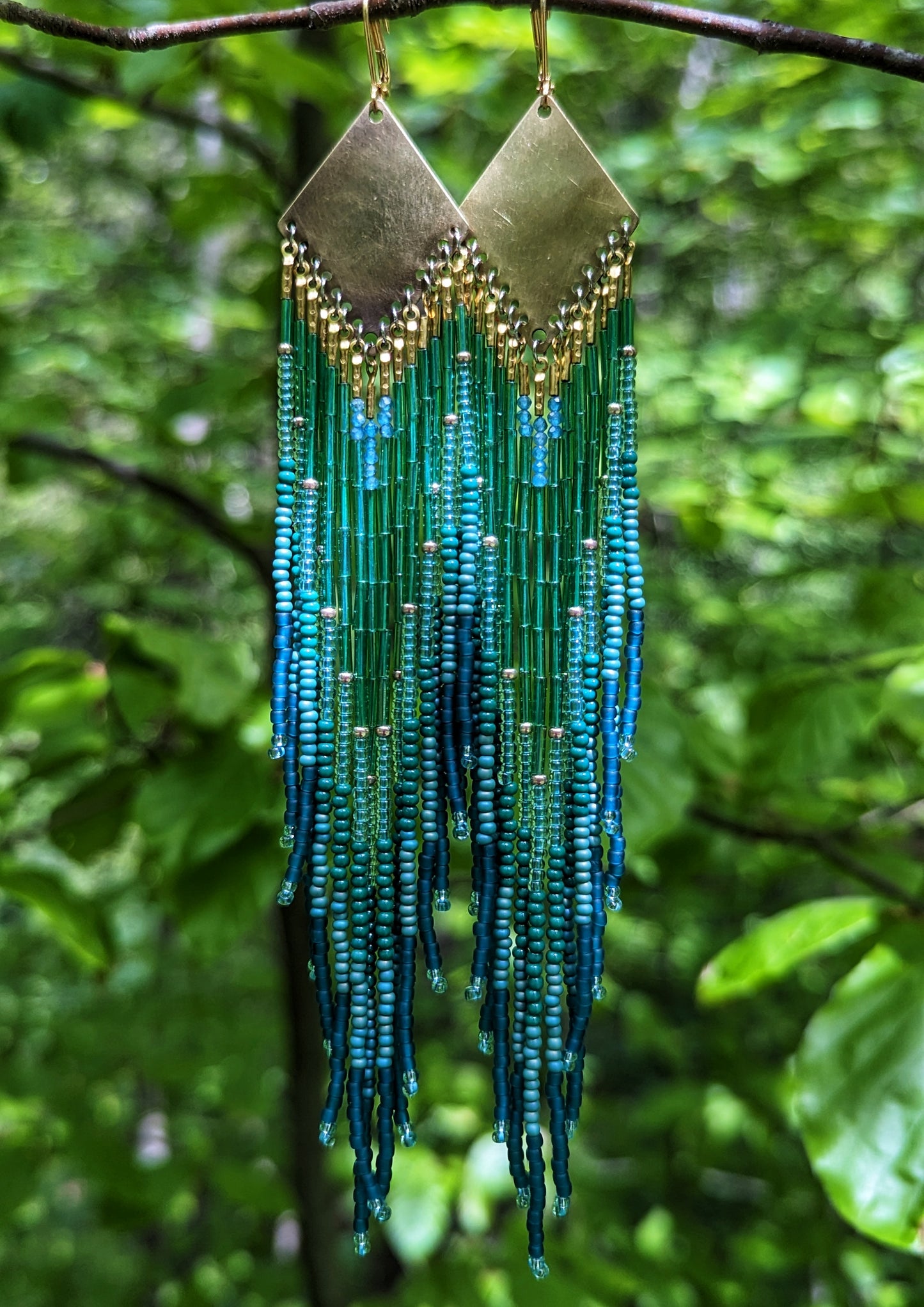 Long beaded earrings by Moon & Milk with deep green, teal, and blue fringe, brass diamond tops, and handcrafted detail inspired by the Swiss forest.
