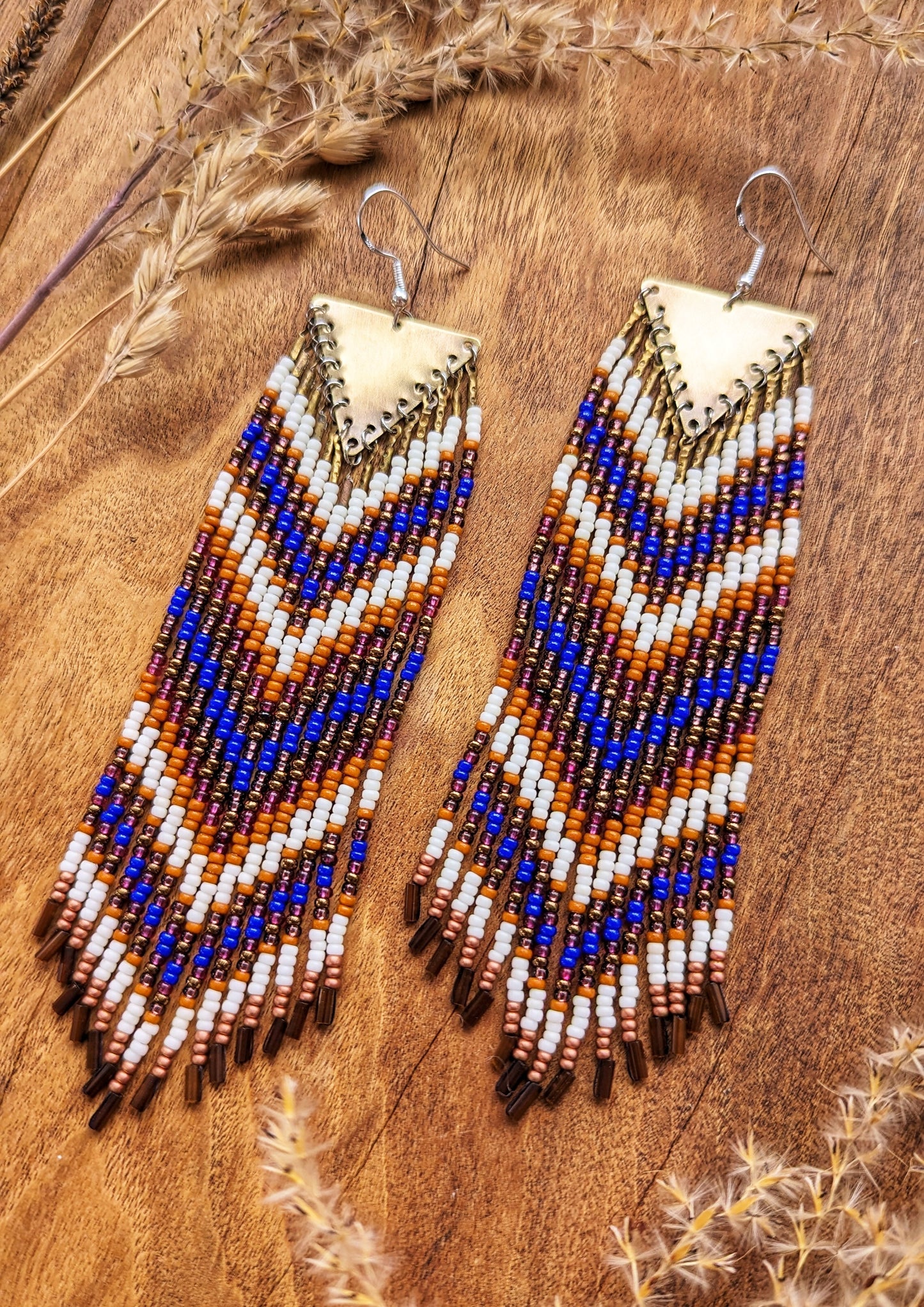 Moon & Milk long native earrings with copper triangle tops and rows of orange, cobalt blue, bronze, and white seed beads on wood background.