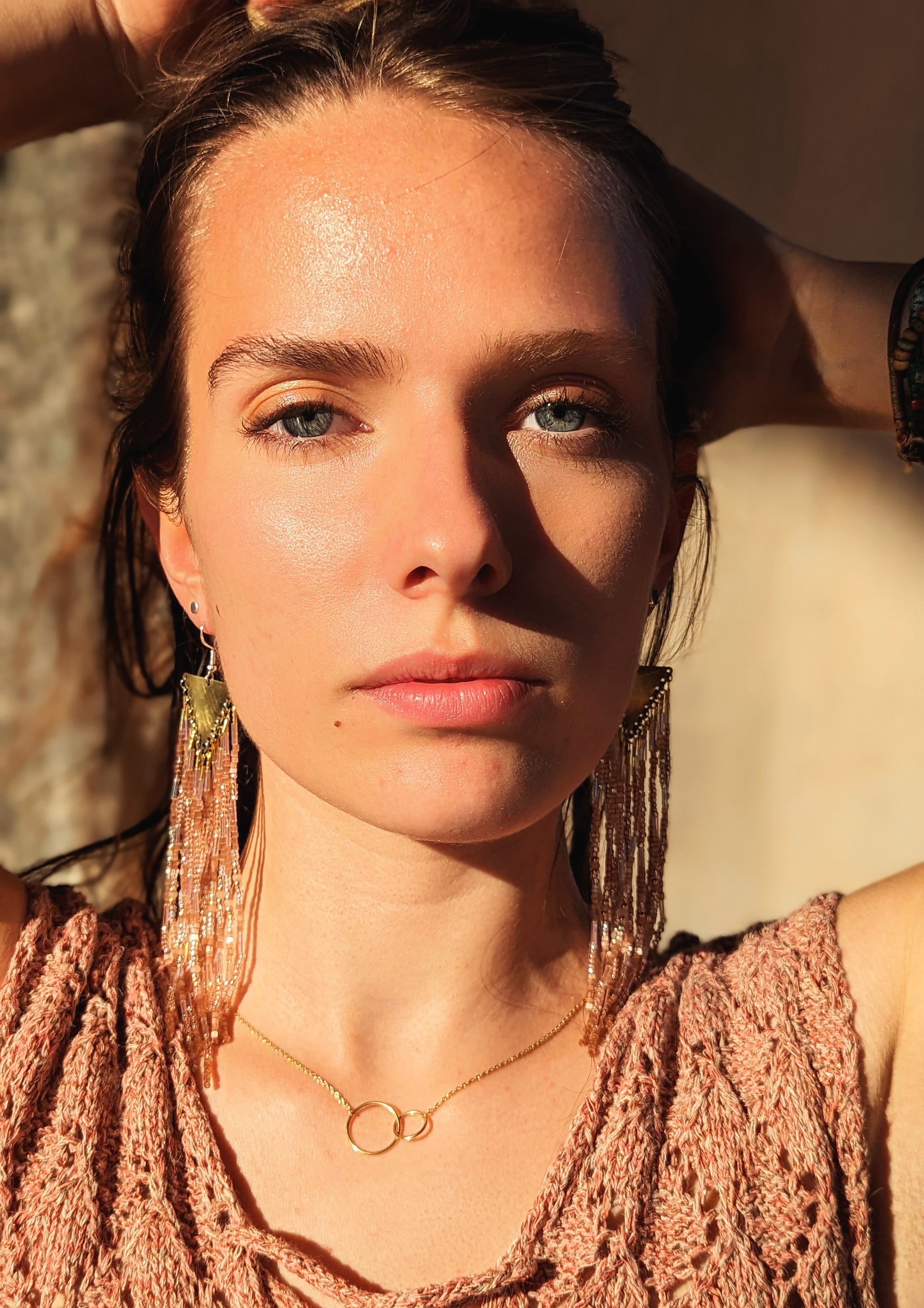 Model wearing Moon & Milk long beaded earrings in warm bronze and peach tones with brass findings, styled with a gold necklace in natural light.