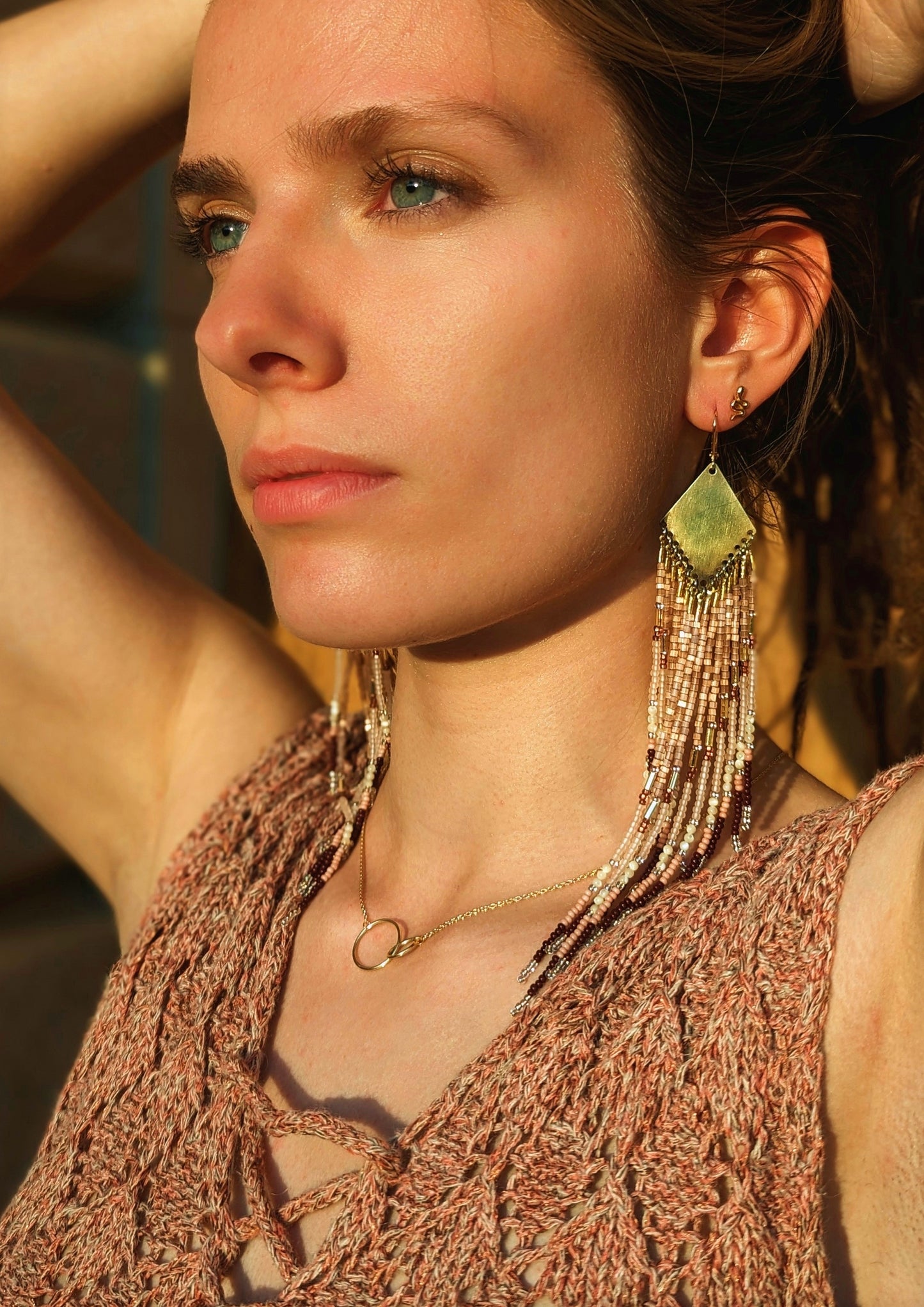 Moon & Milk long native beaded earrings in beige, blush, and bronze tones, worn by a woman in sunlight with a gold double-circle necklace.