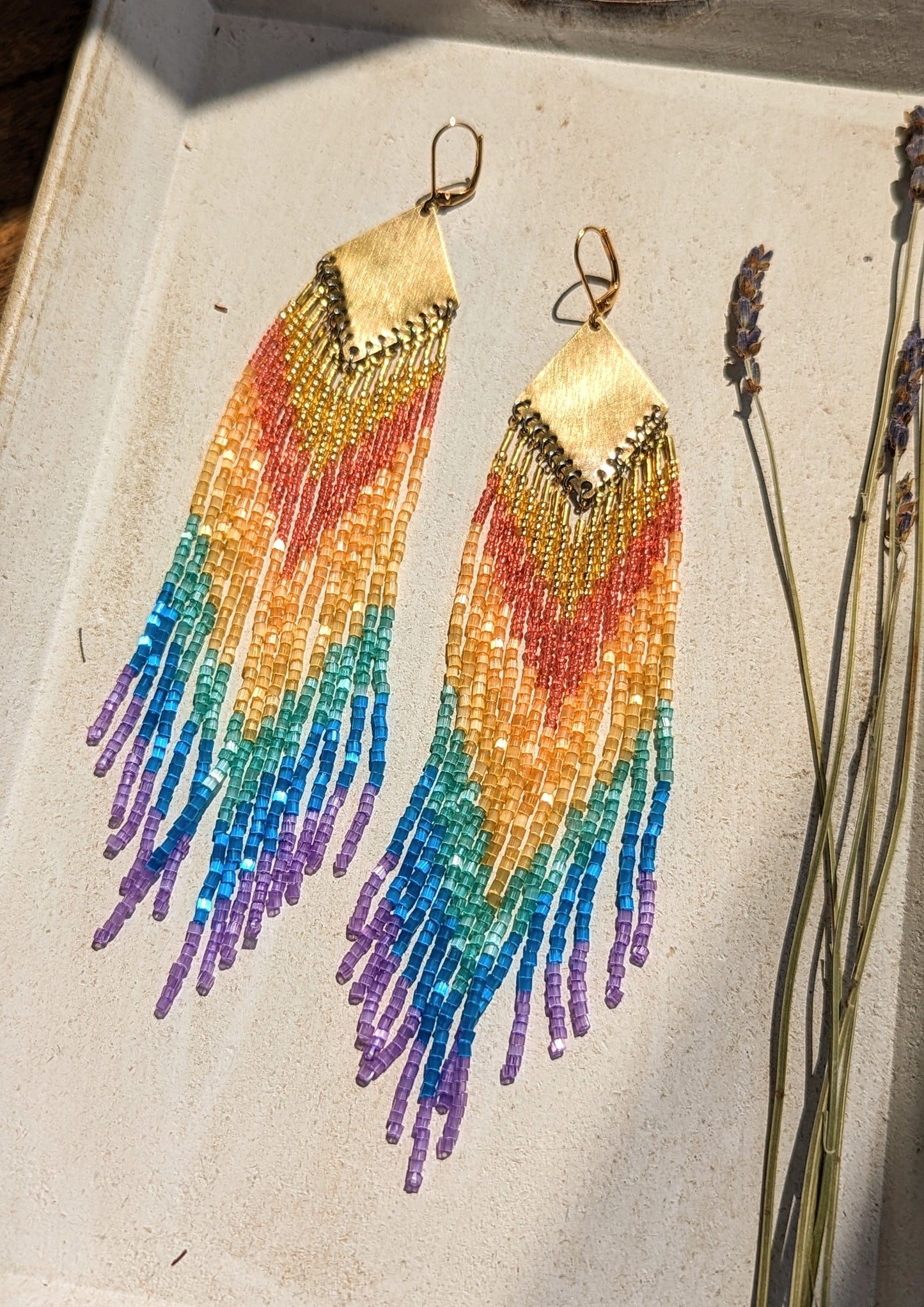 Handcrafted beaded earrings by Moon & Milk featuring vibrant glass beads in rainbow hues with brass accents, showcasing a boho and colorful design.